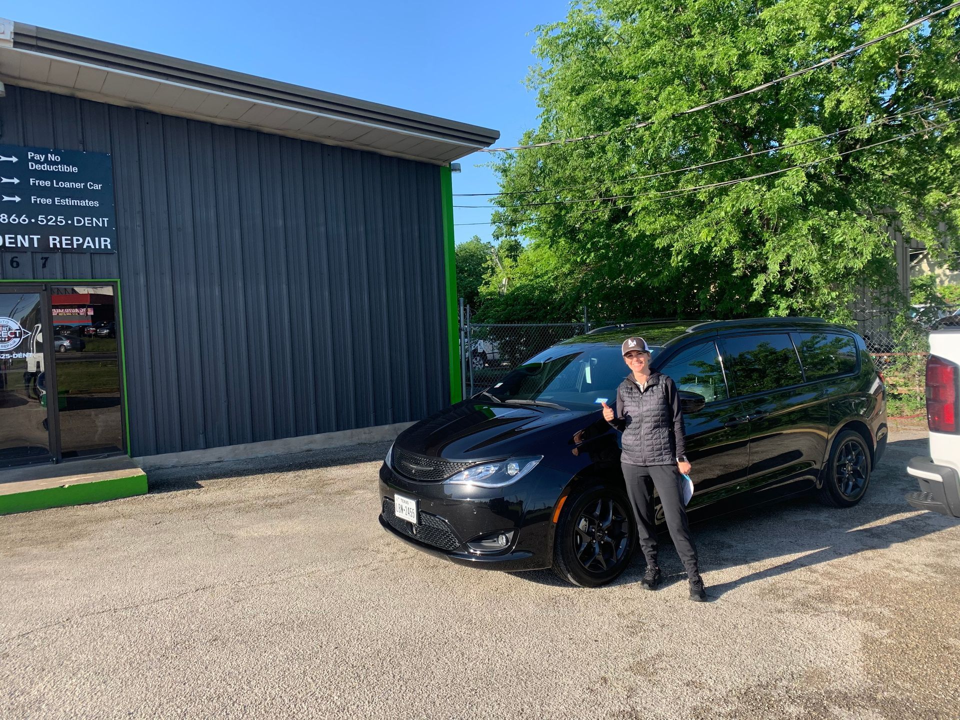 A woman is standing next to a black car in front of a building.
