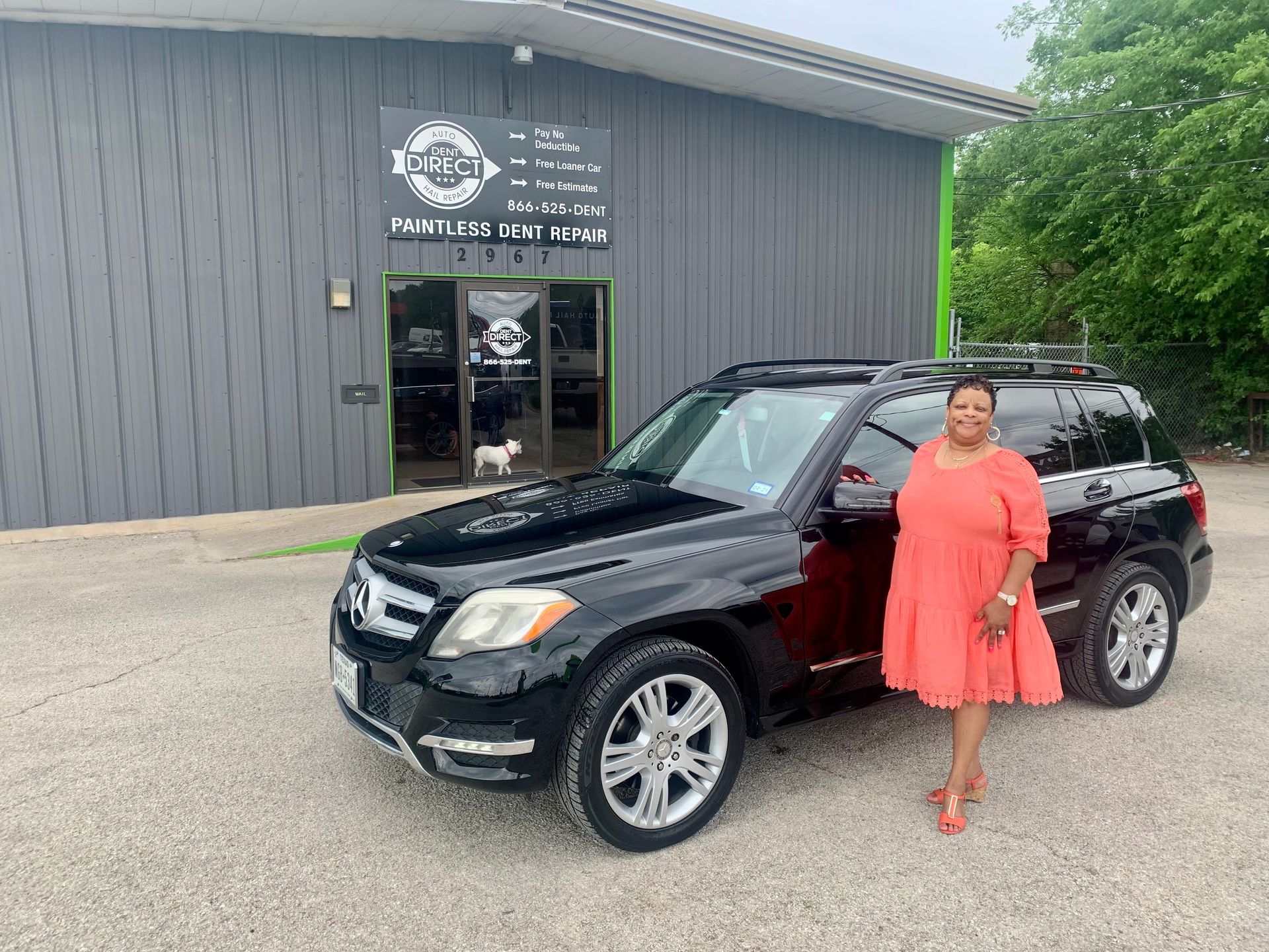 A woman in a red dress is standing in front of a black suv.