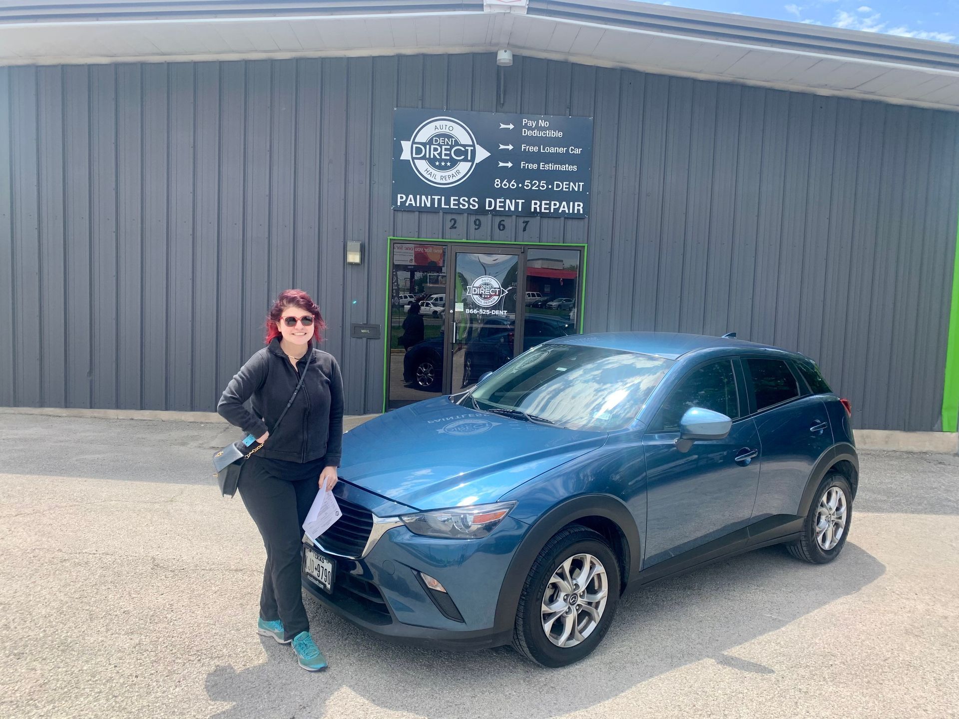A woman is standing in front of a blue car.