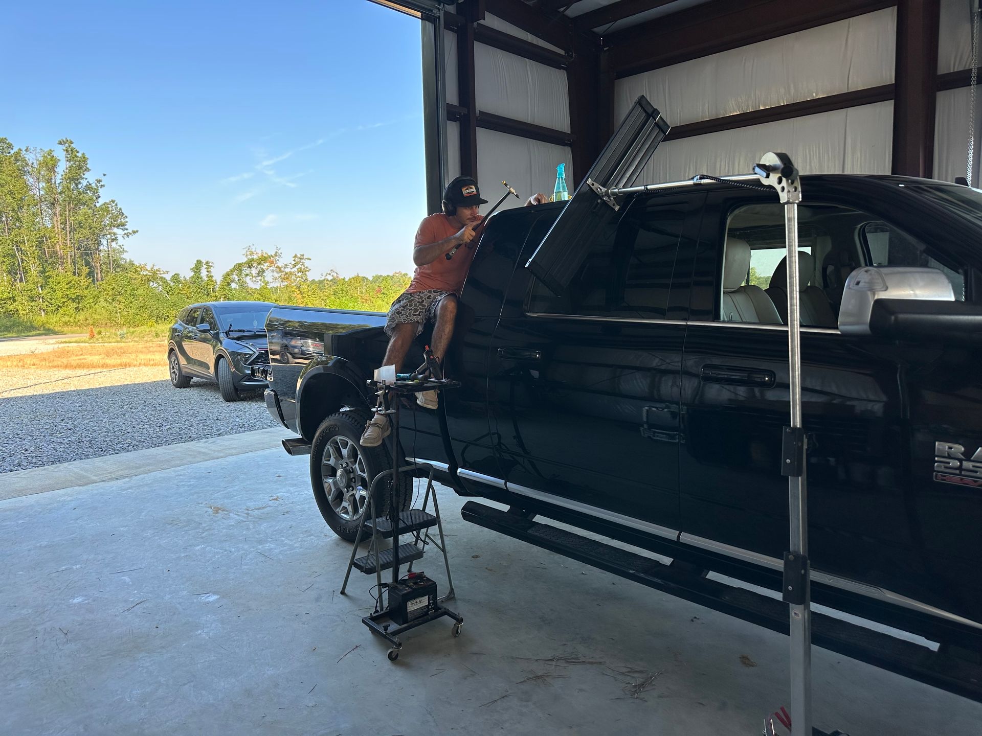 A man is standing on a ladder next to a truck in a garage.