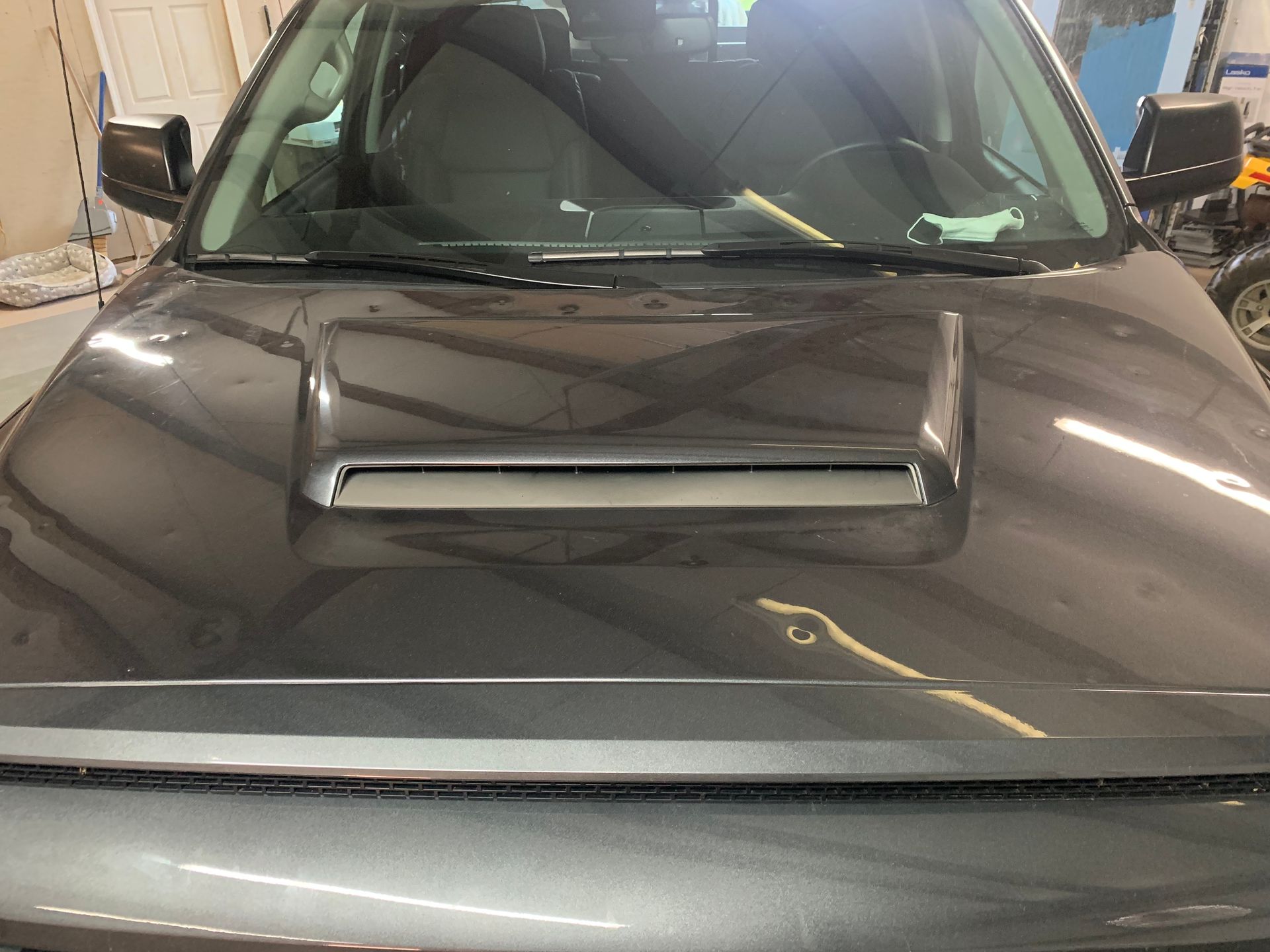 A gray car with a hood scoop is parked in a garage.