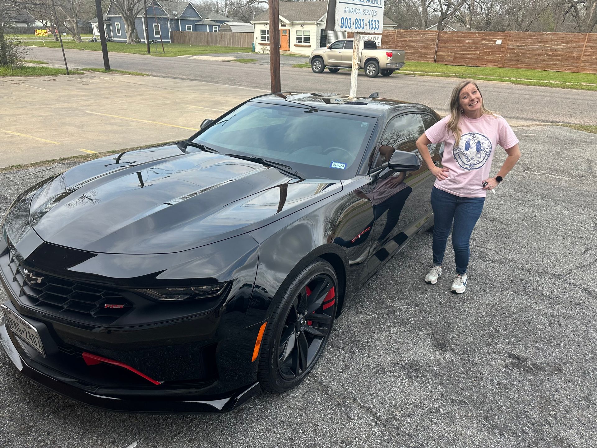 A woman is standing next to a black car in a parking lot.