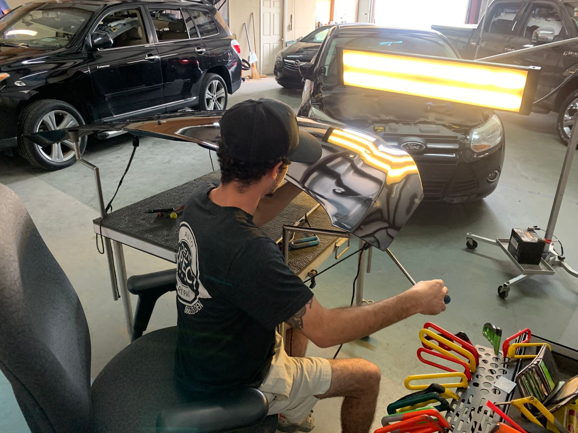 A man is sitting in a chair working on a car in a garage.