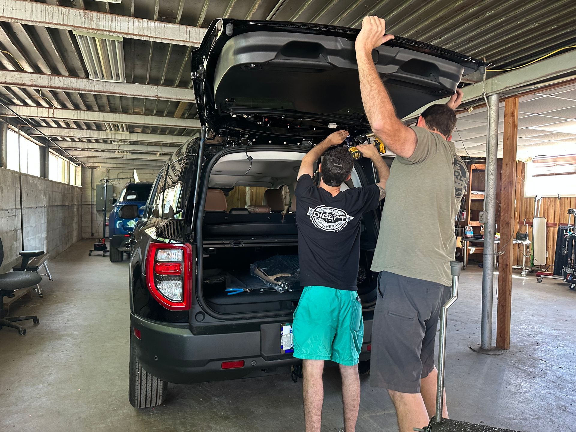 Two men are working on the trunk of a car in a garage.
