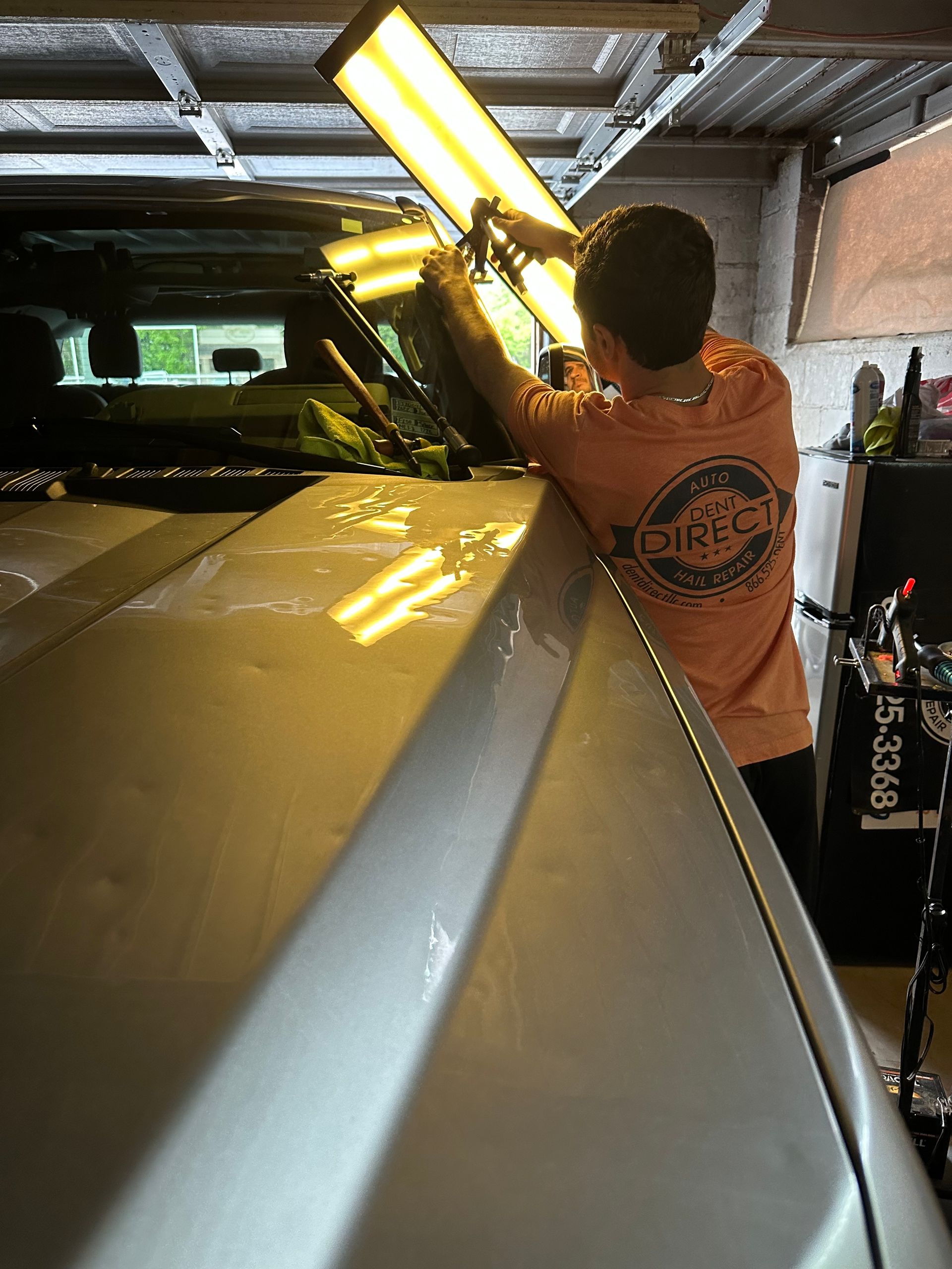 A man is working on the roof of a car in a garage.