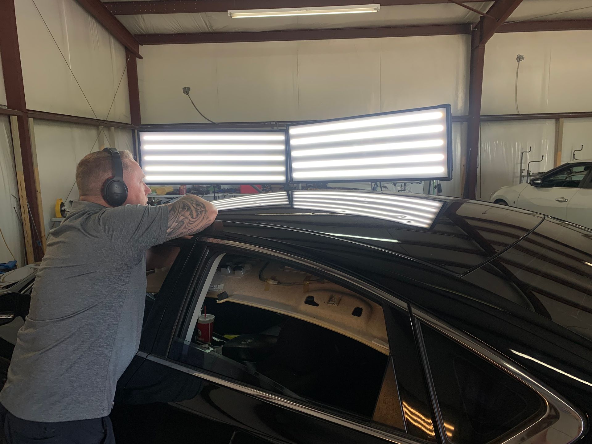 A man wearing headphones is working on the roof of a car.