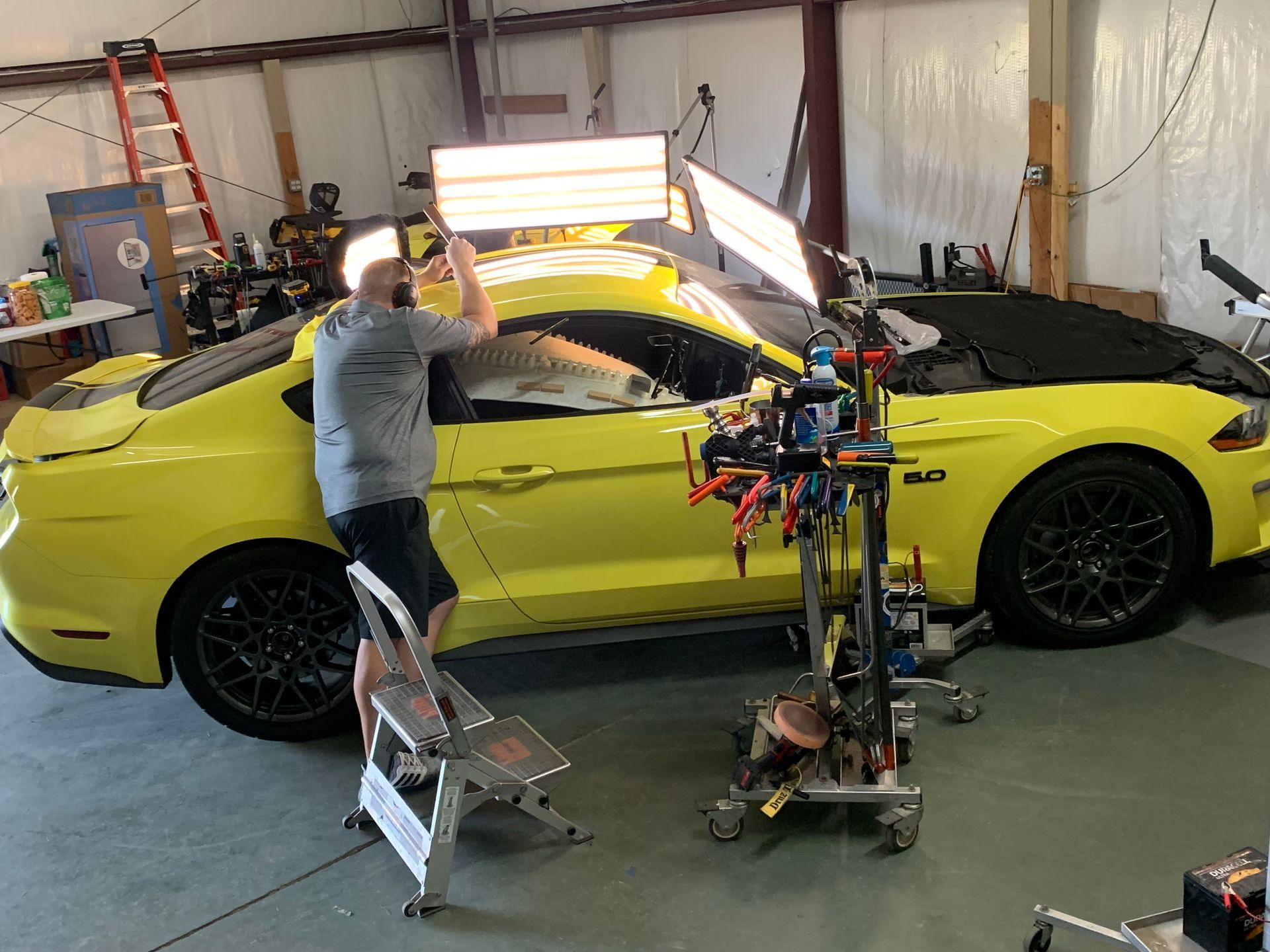 A man is working on a yellow mustang in a garage.
