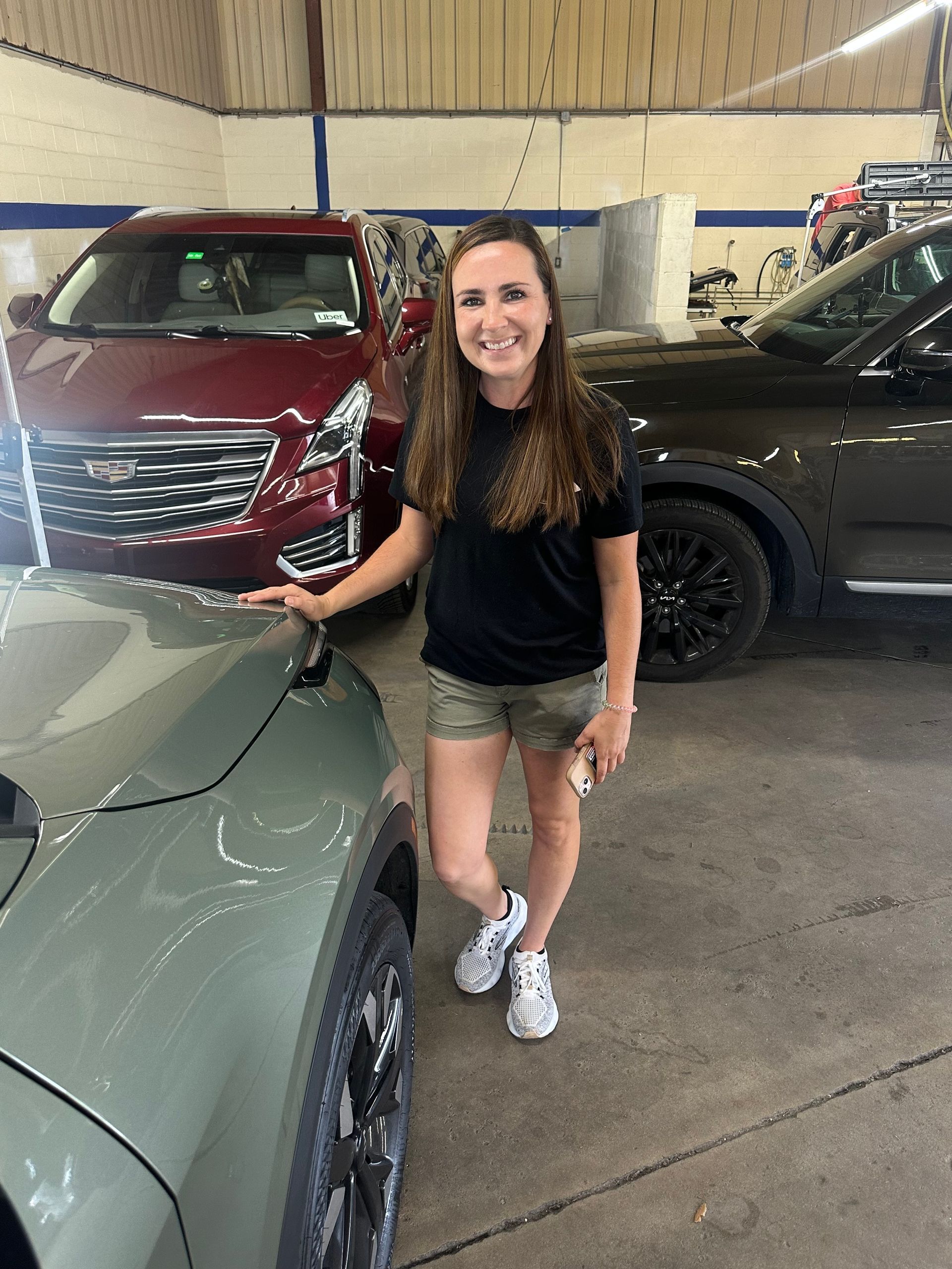 A woman is standing next to a car in a garage.