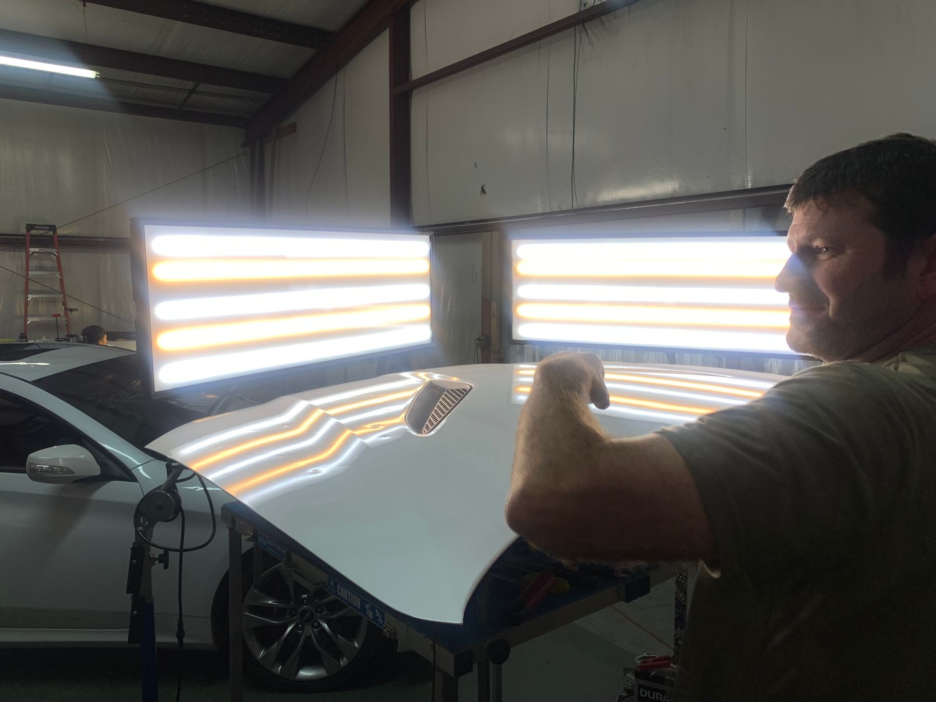 A man is working on the hood of a car in a garage.