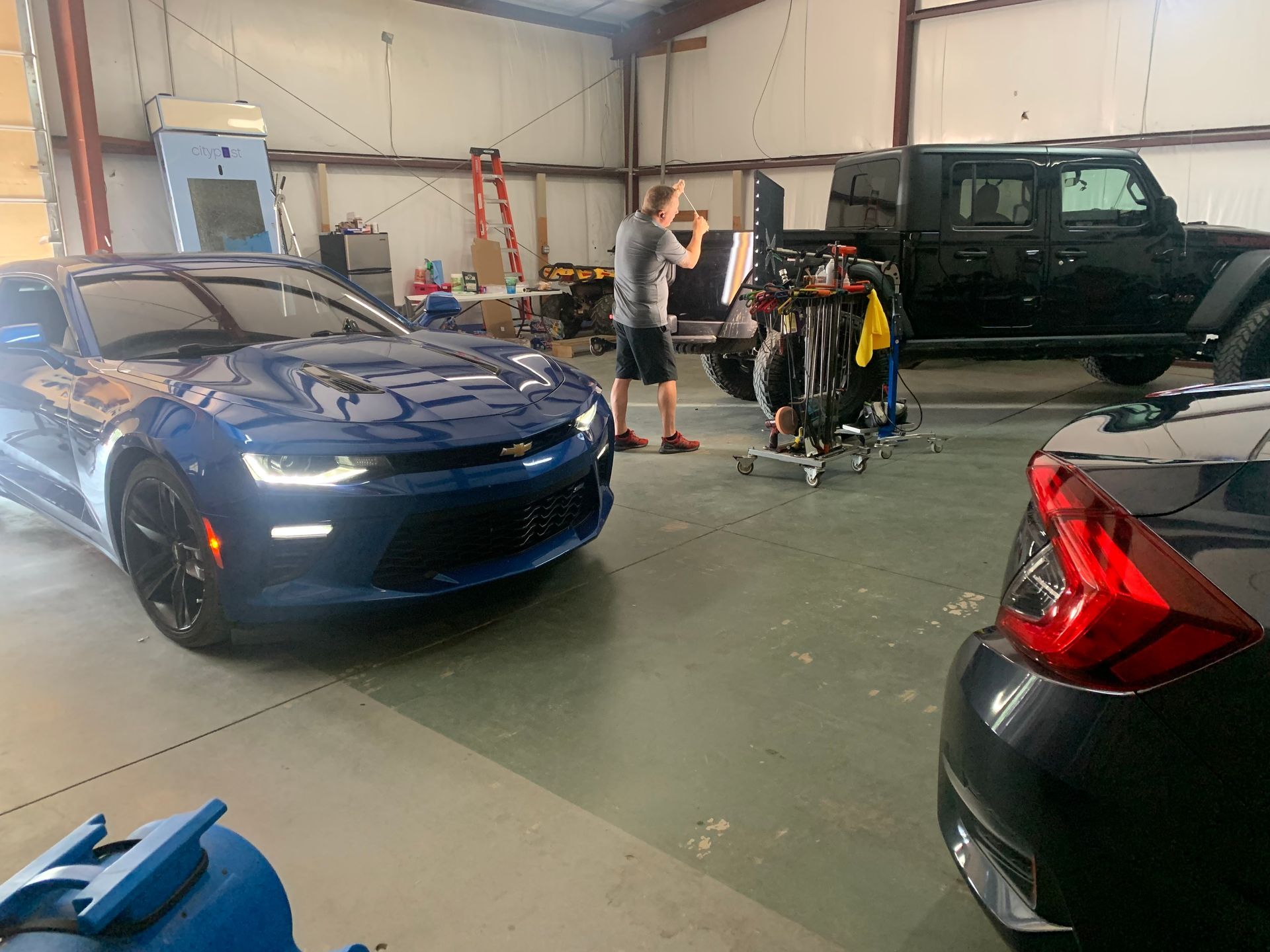 A man is standing next to a blue car in a garage.