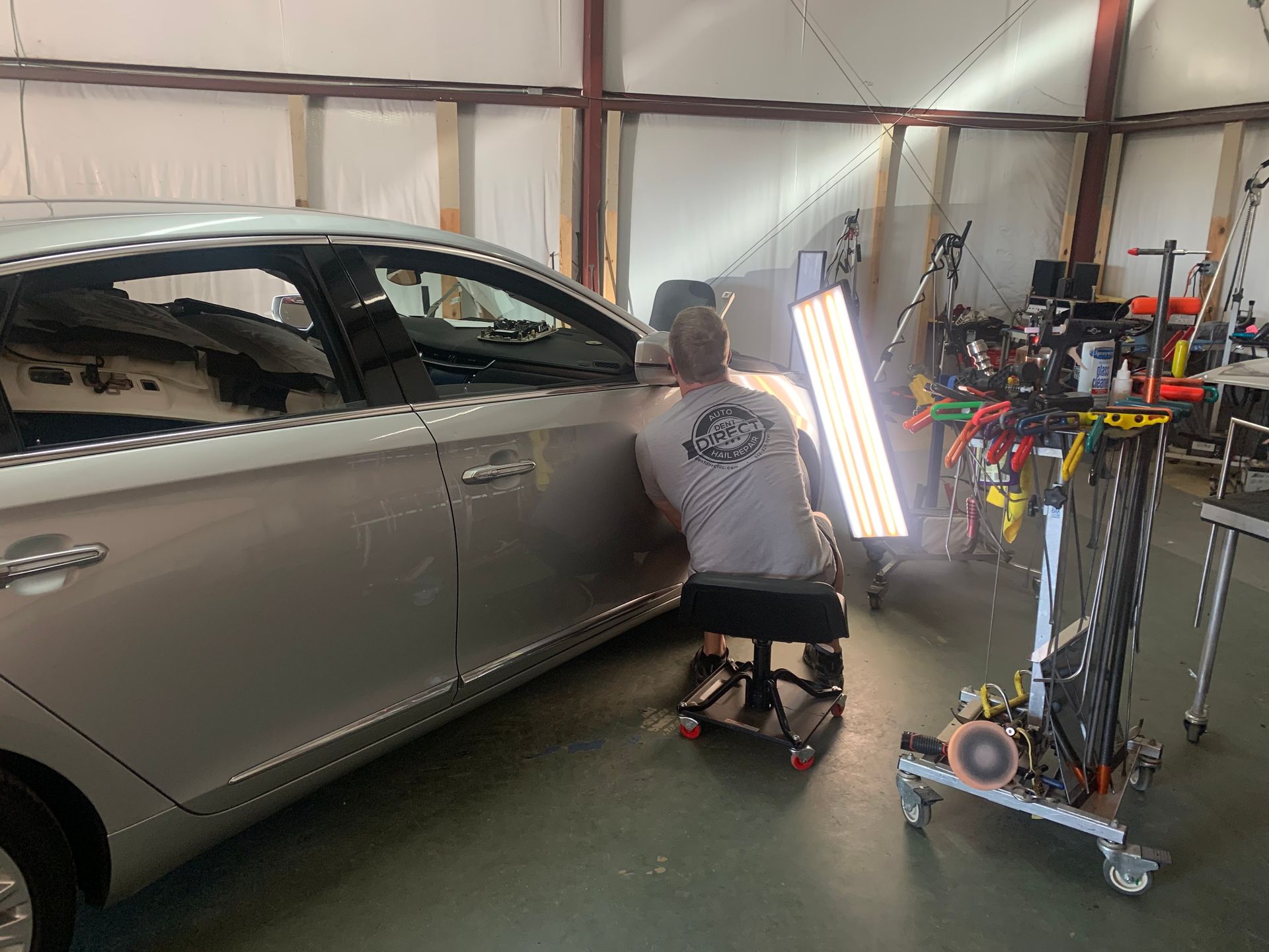 A man is sitting on a stool in front of a car in a garage.
