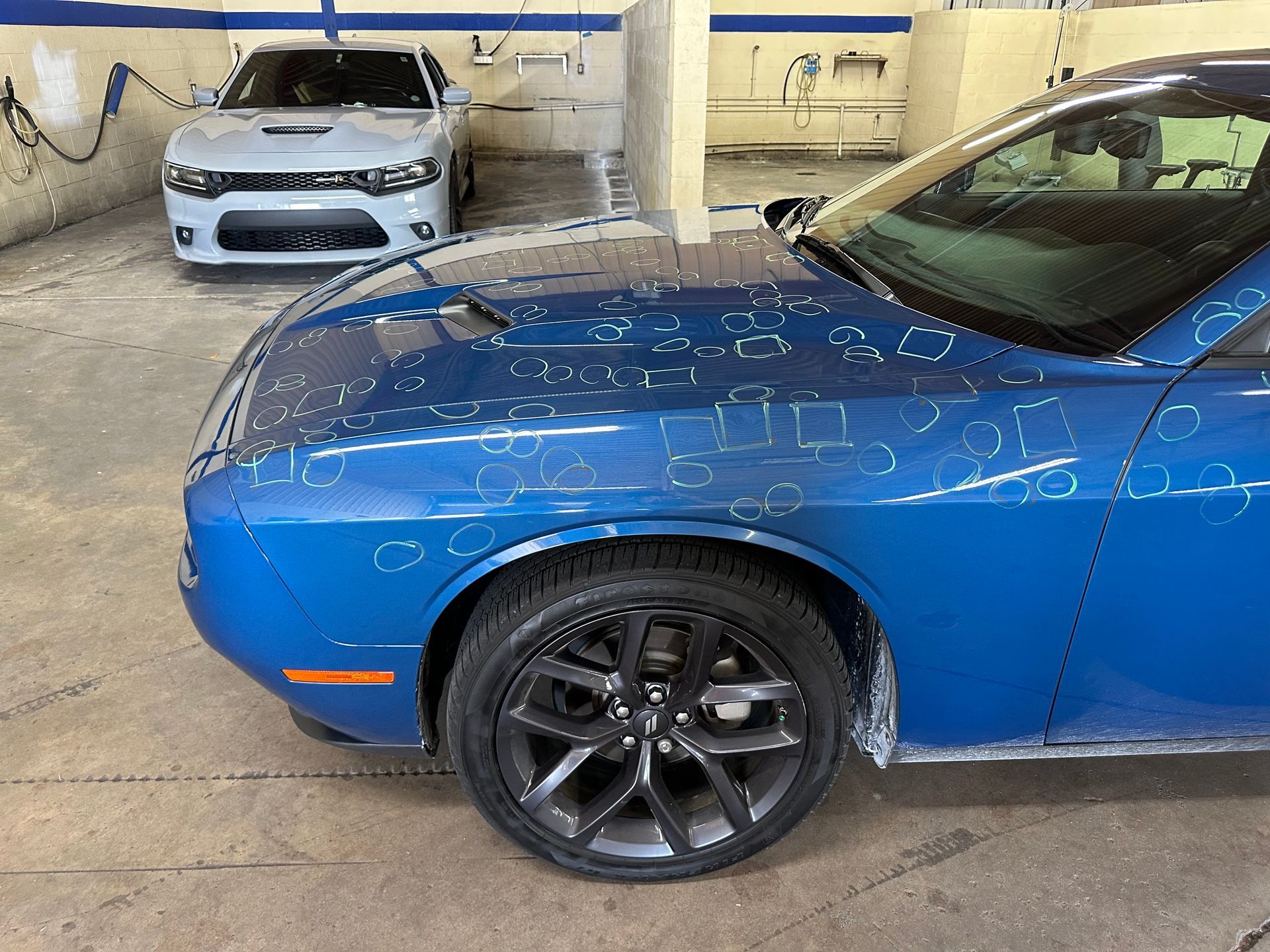 A blue car is parked in a garage next to a white car.