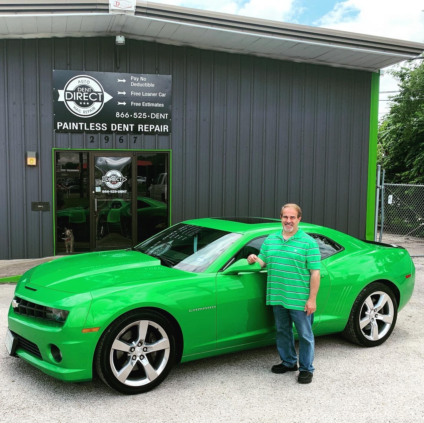 A man is standing next to a green car in front of a building.