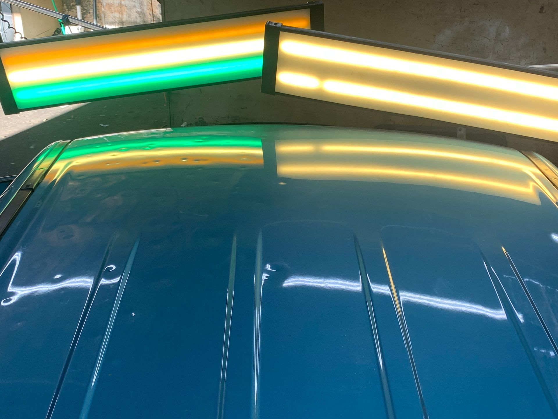 The roof of a blue car is being repaired with green and yellow lights.