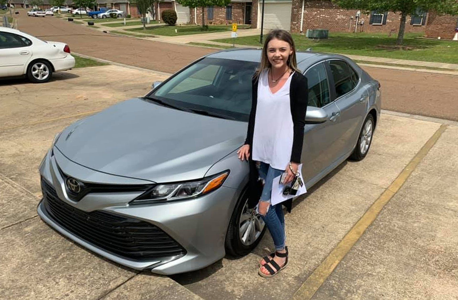 A woman is standing next to a silver car in a parking lot.