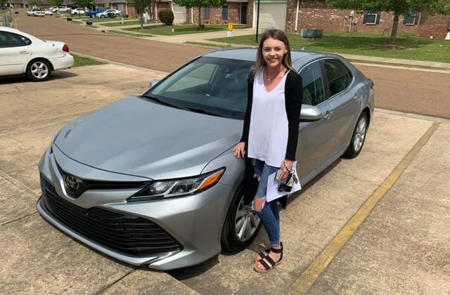 A woman is standing next to a silver car in a parking lot.