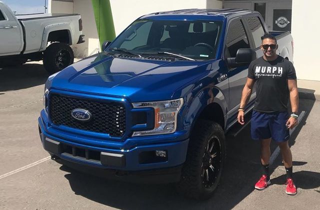 A man is standing in front of a blue ford truck.