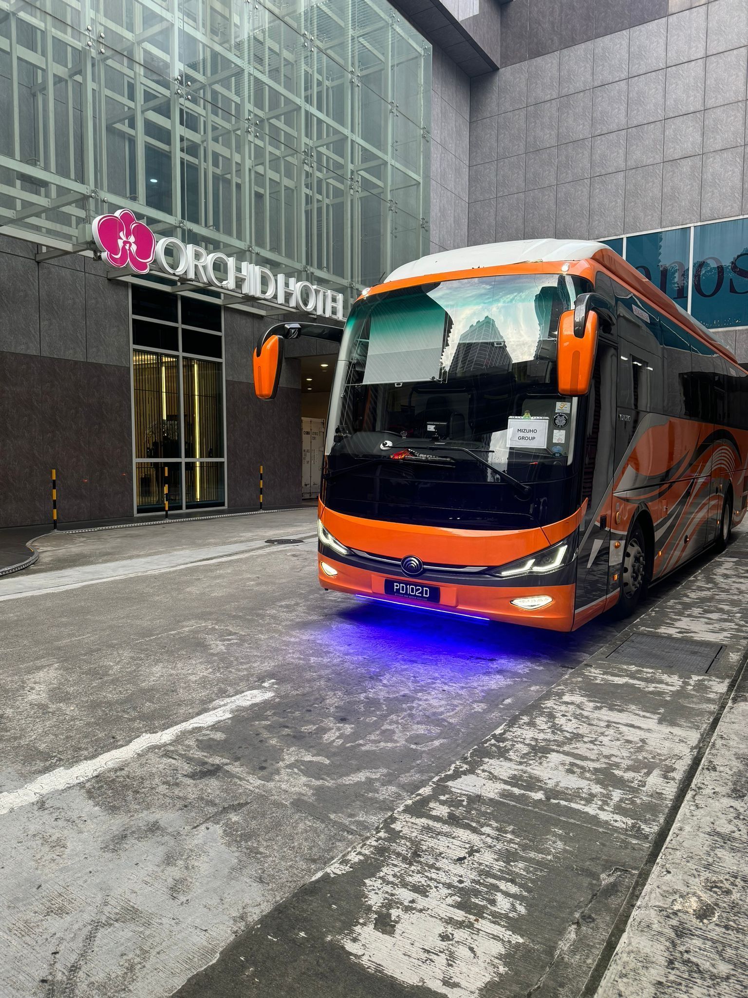 Orange tour bus parked in front of the Orchid Hotel building.