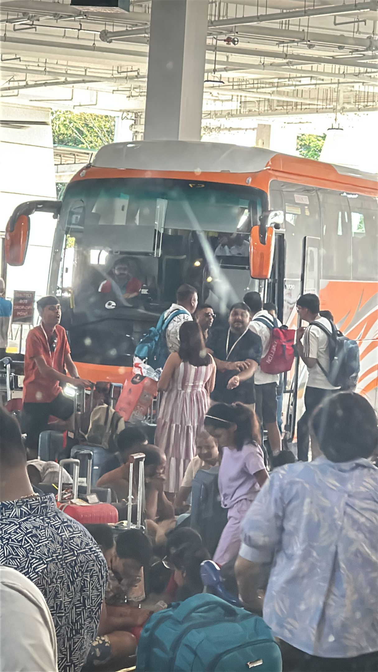 People with luggage near an orange bus at a transportation hub.