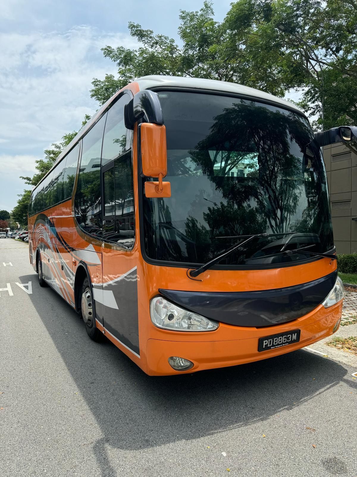 Orange and black coach bus parked on a road in front of trees.