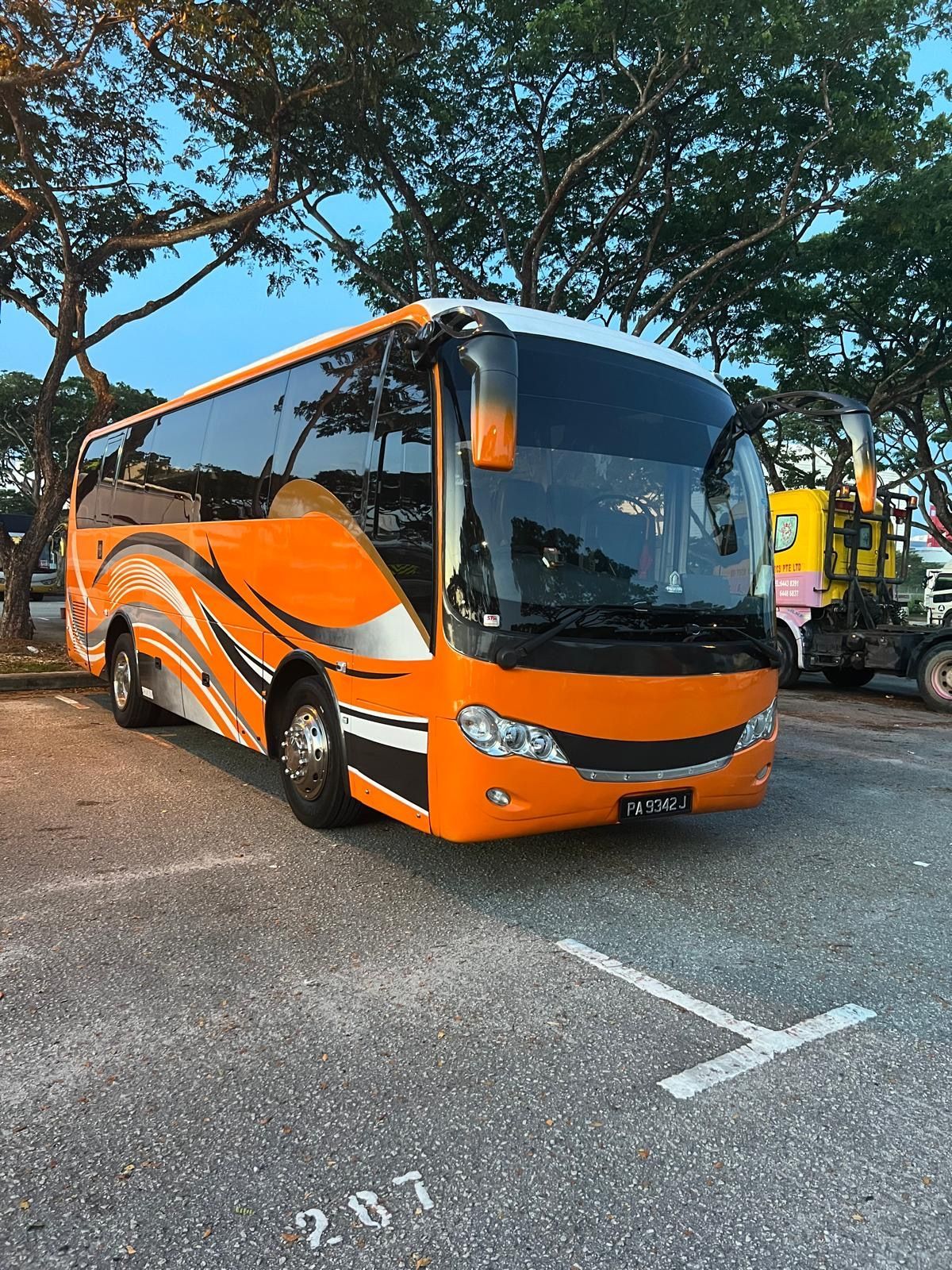 Orange and black coach bus parked in a lot under trees at dusk