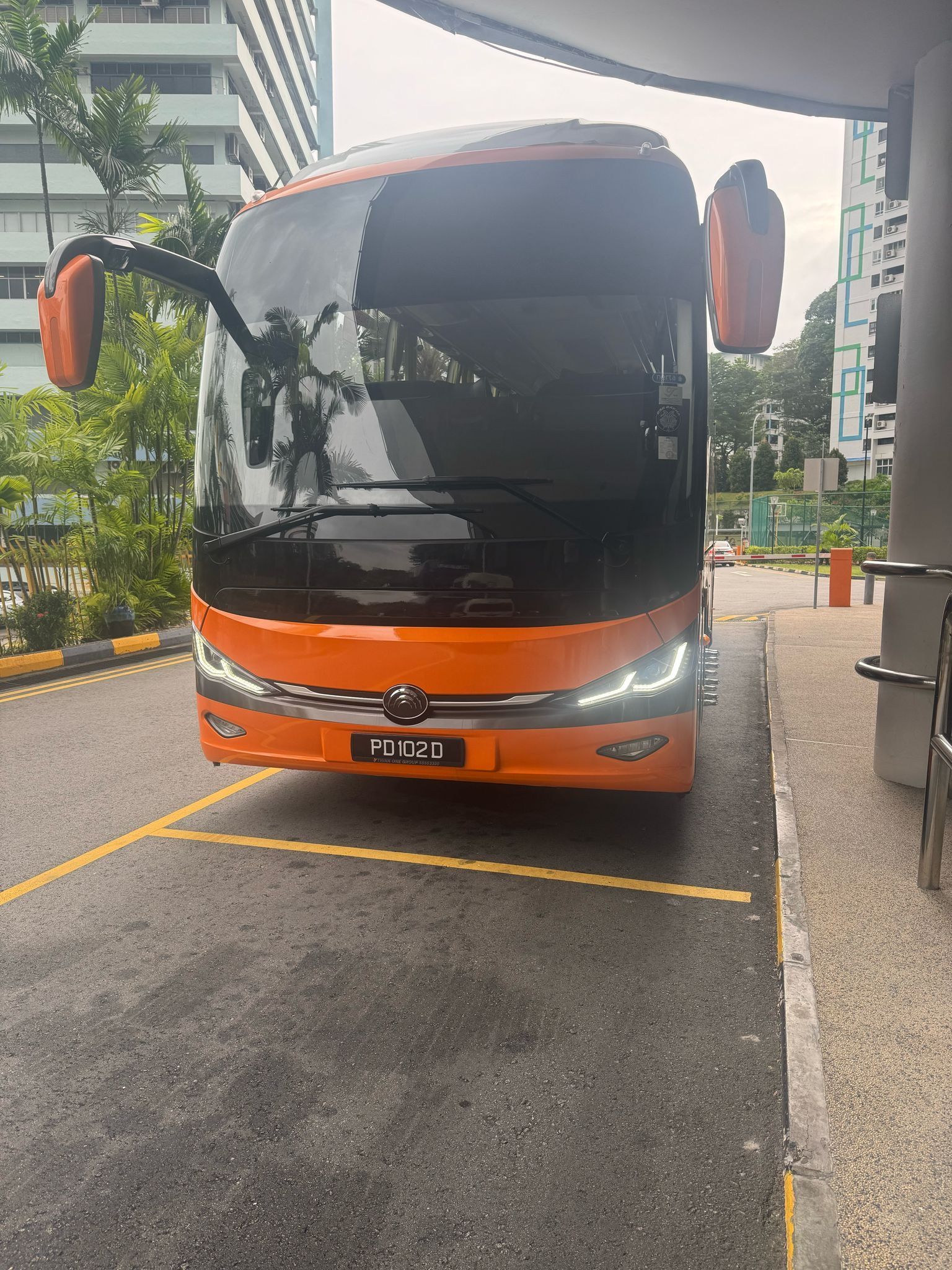 Orange and black coach bus parked at a curb under a covered drive-through.