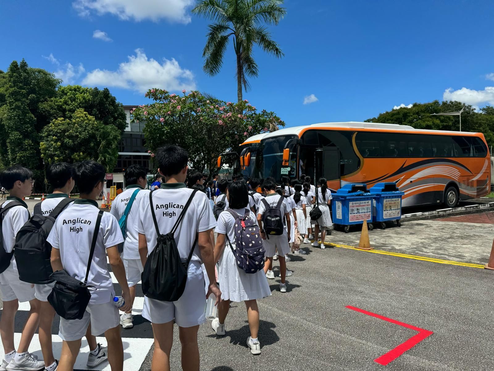Students in white uniforms walking toward an orange bus in a sunny parking lot