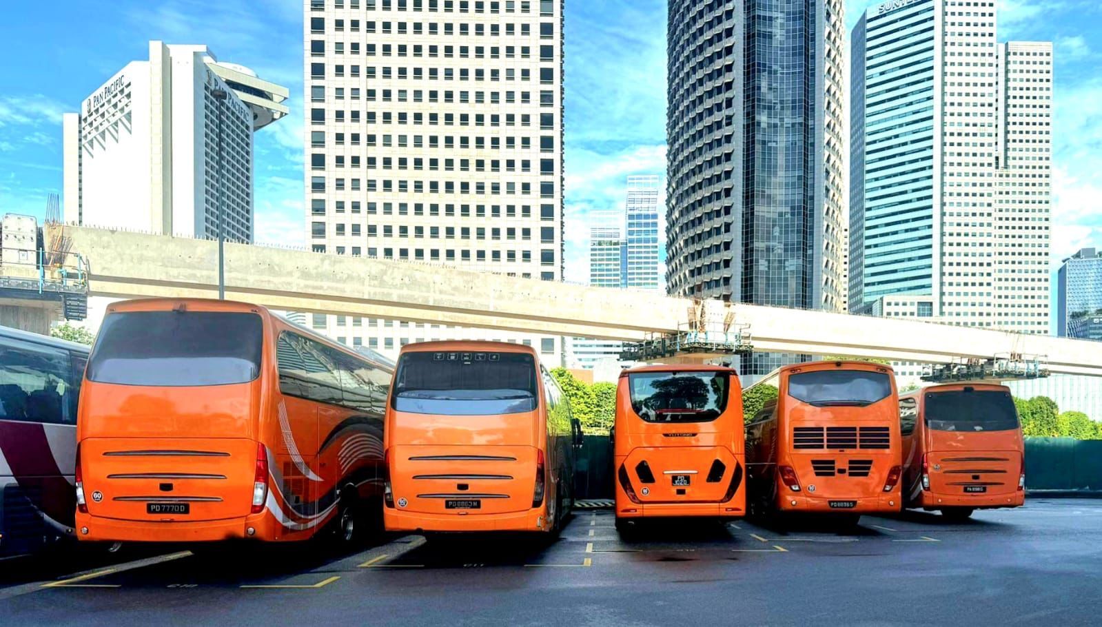 Orange buses parked in a lot, with skyscrapers in the background.