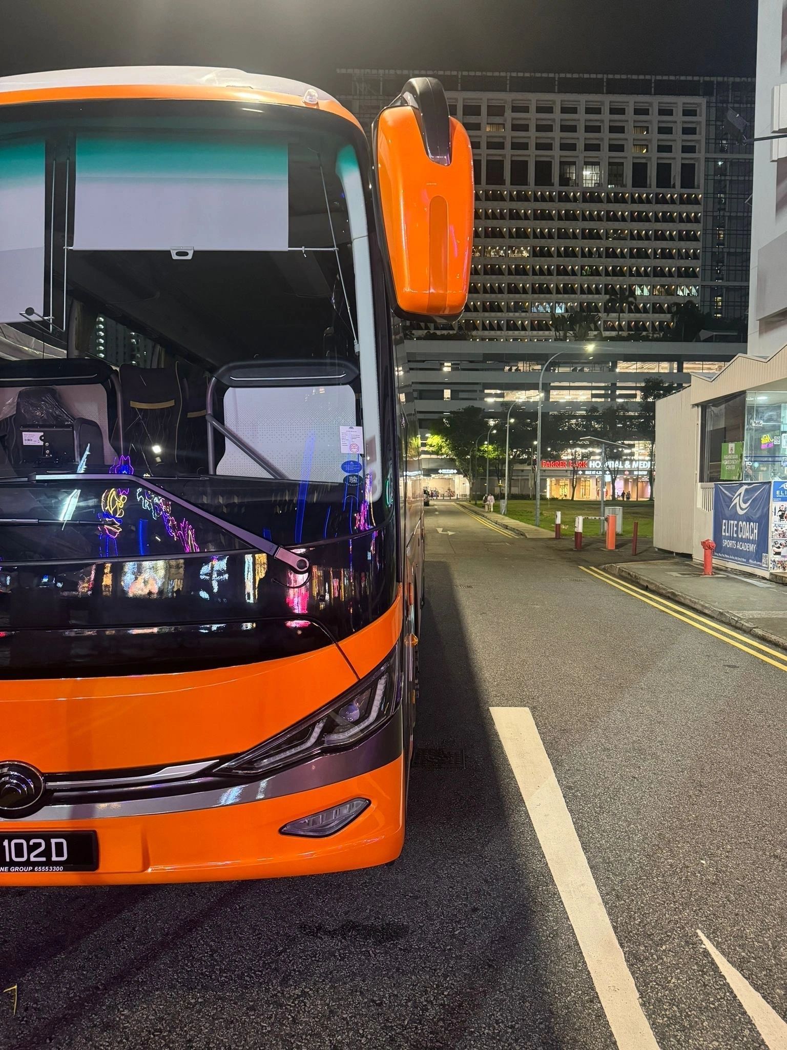 Orange bus parked on a city street at night, buildings in the background.