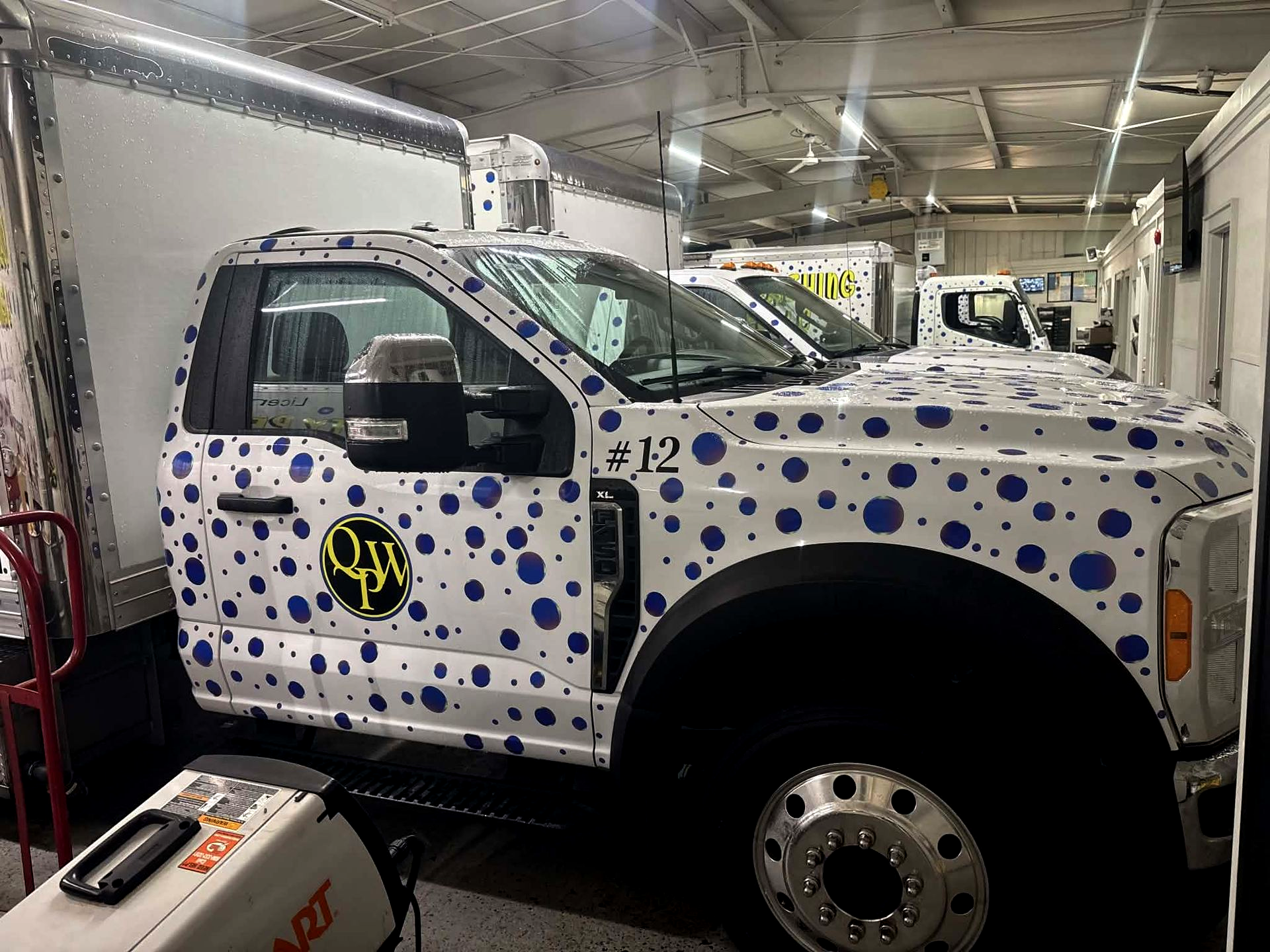 White truck covered in blue dots inside a garage, with a yellow-and-black logo on the door