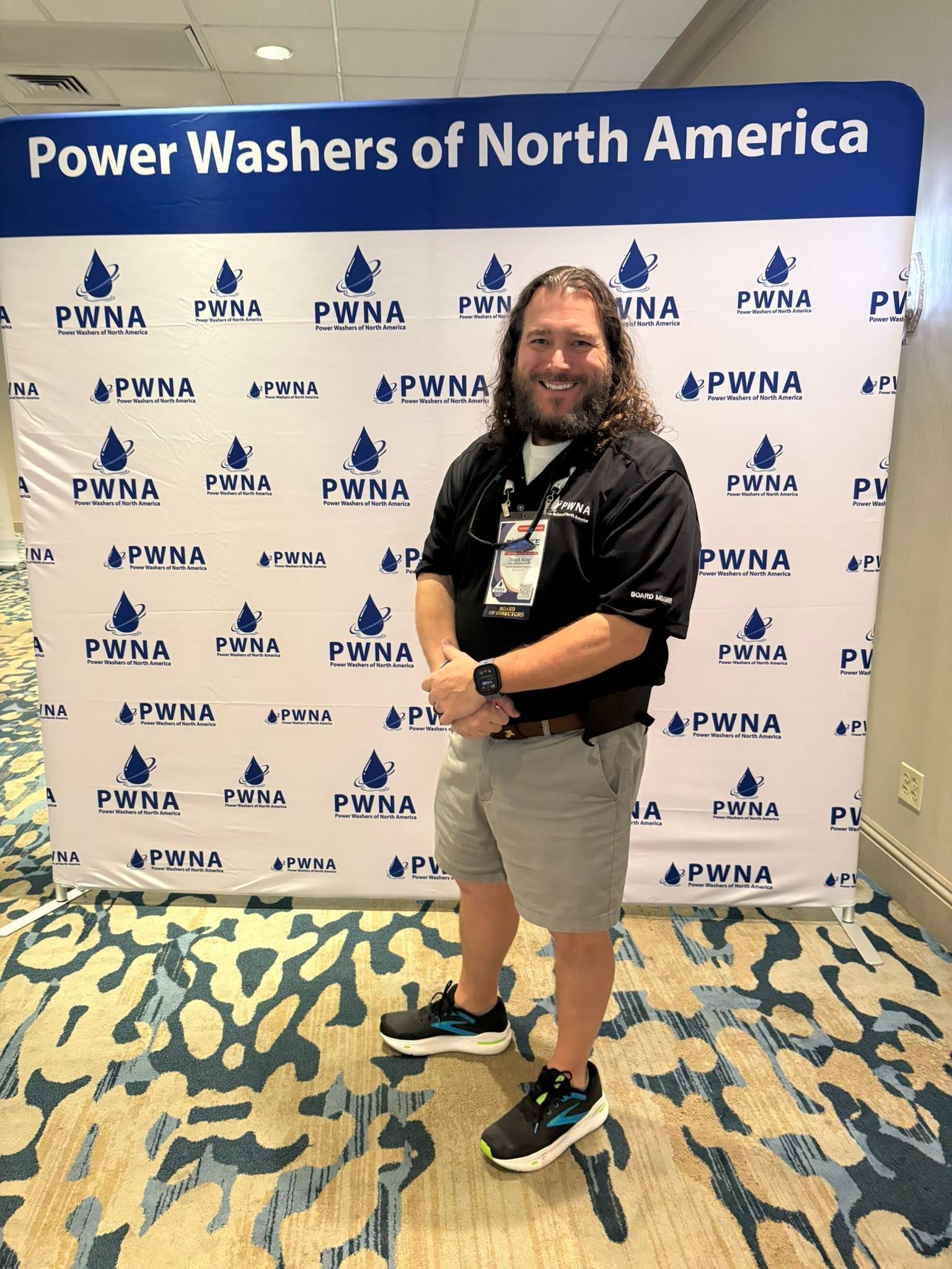 Person posing at a Power Washers of North America event backdrop, holding an award and smiling.