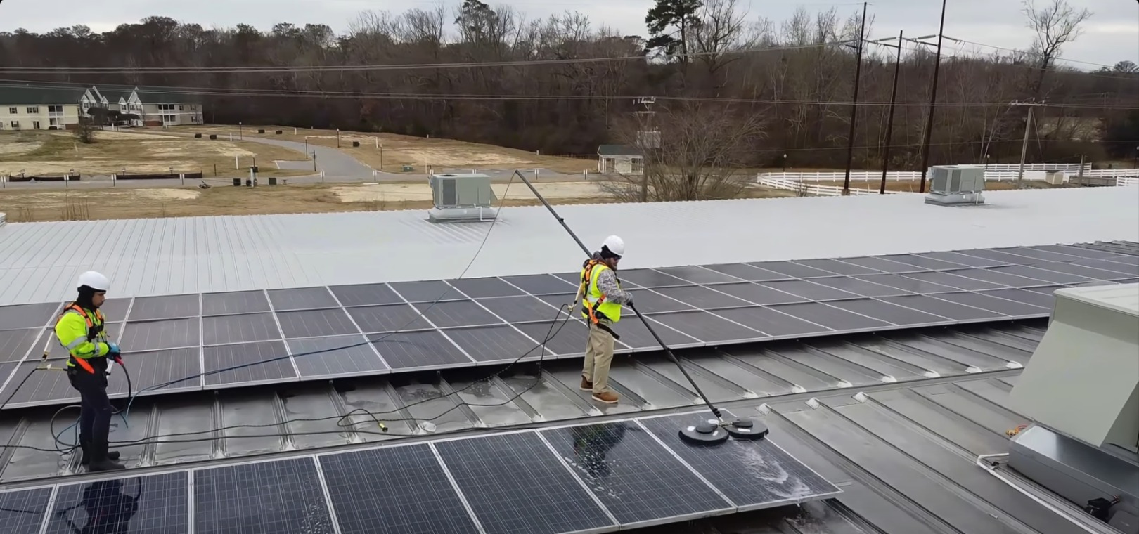 Workers in safety vests install solar panels on a large rooftop.