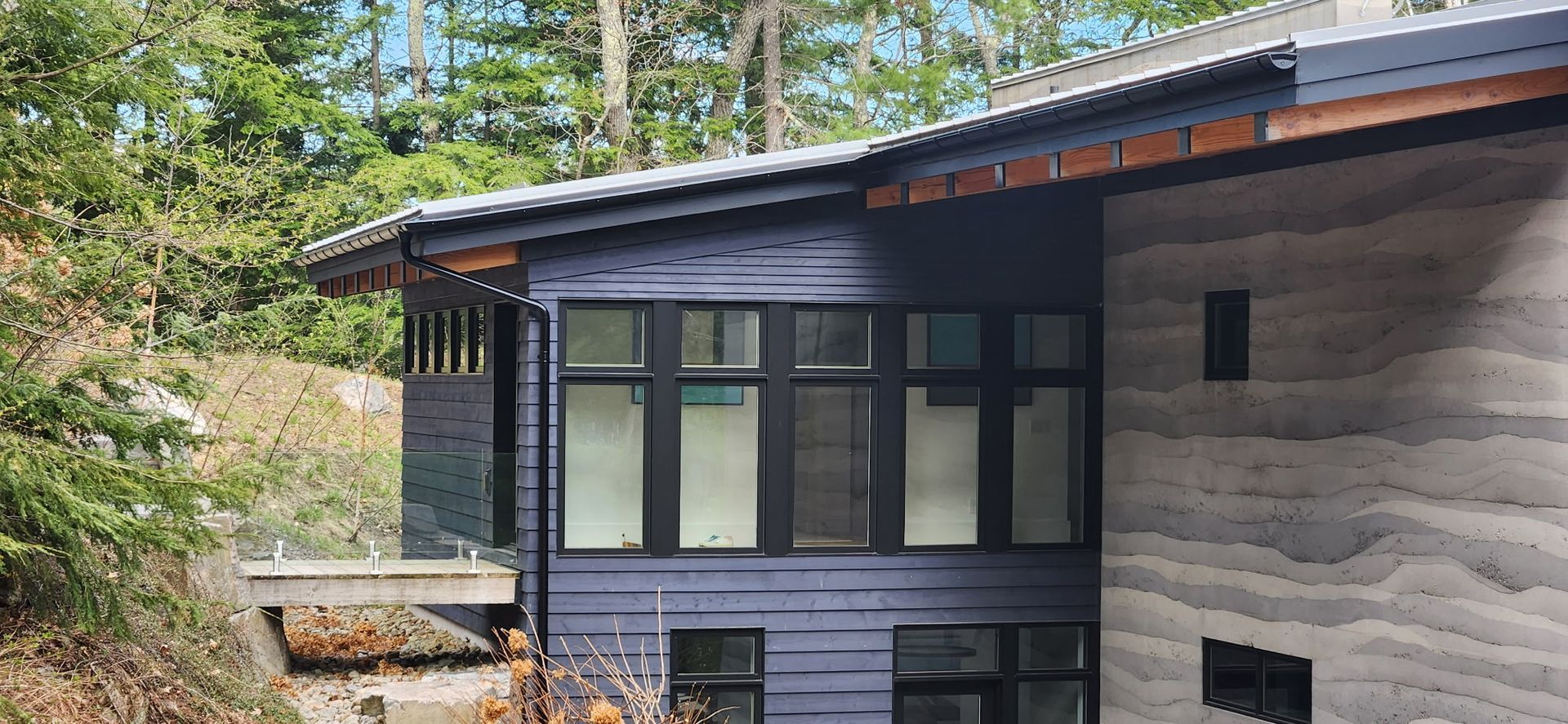 Modern house exterior with large windows and wood siding, surrounded by trees