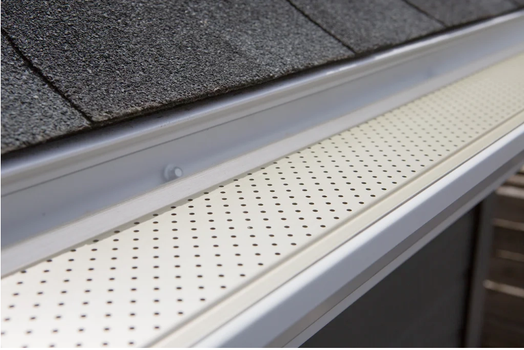 White roof gutter guard beside dark gray shingles on a sloped roof