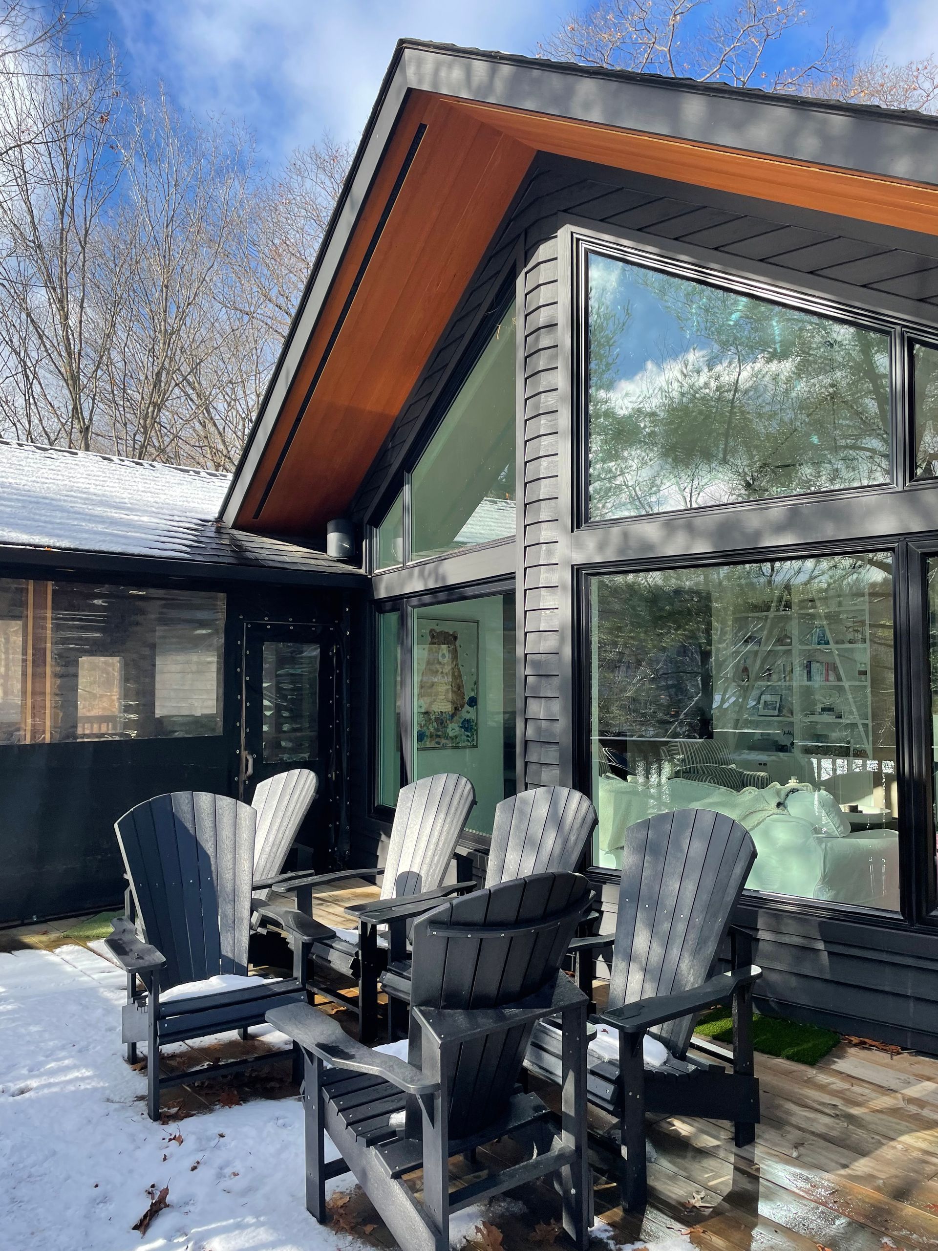 Snowy patio with black chairs beside a modern glass house and large windows
