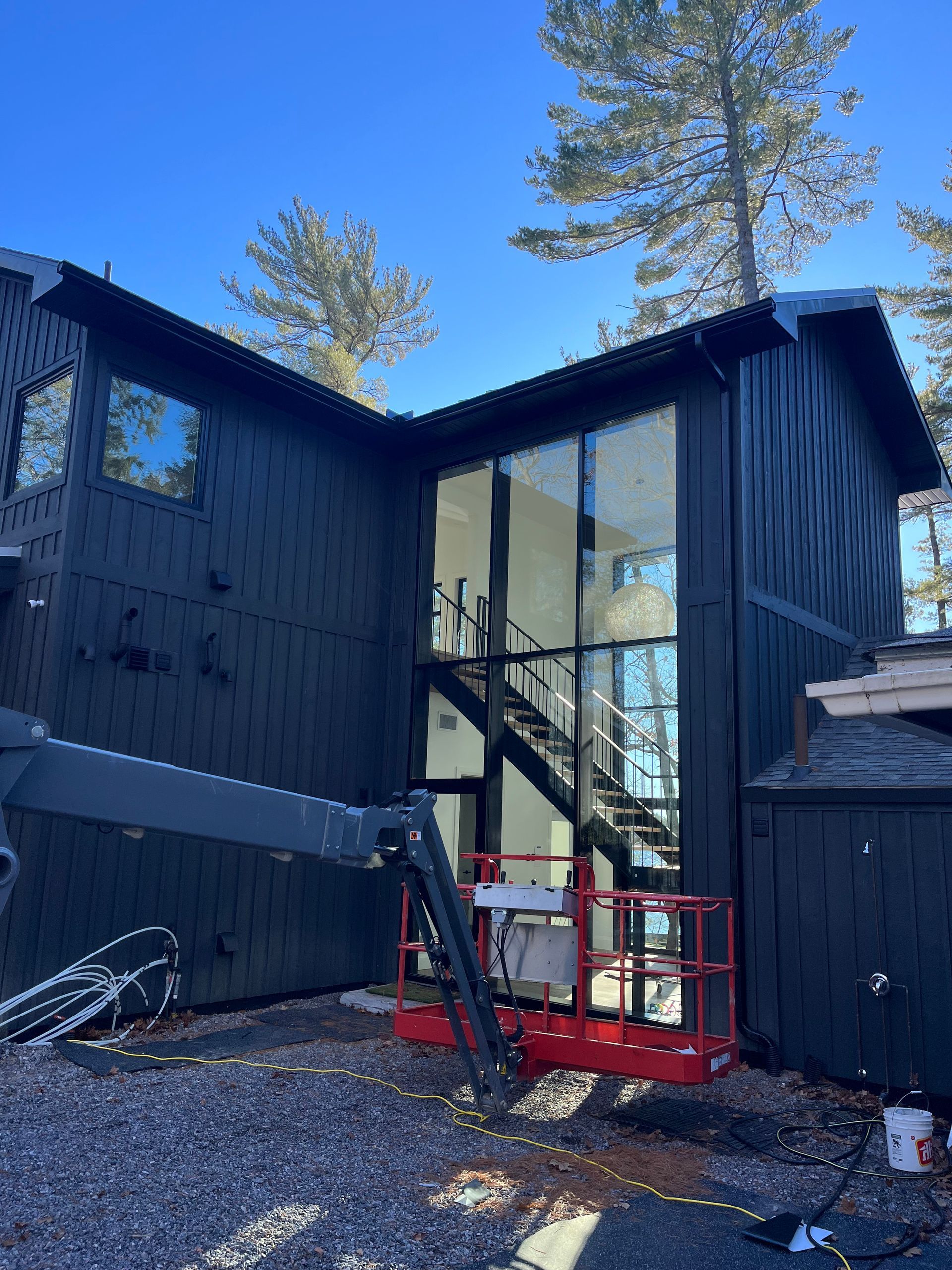 Modern black house with tall glass entry and red lift on gravel driveway under blue sky
