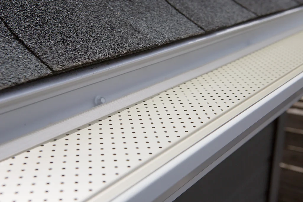 Perforated white gutter guard along a roof edge beneath dark shingles