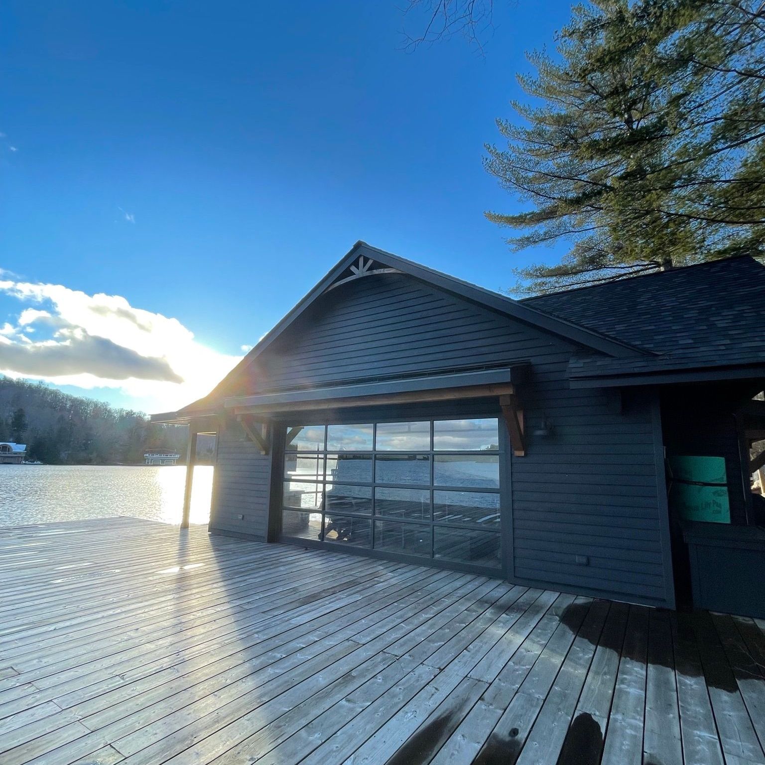 Snowy lakeside deck beside a gray cabin under a bright blue sky at sunset