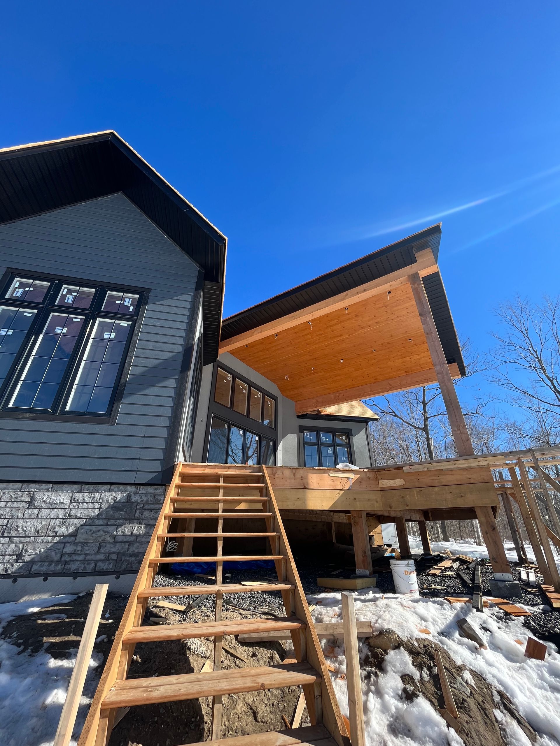 Modern house with wooden deck and stairs in snowy yard under a clear blue sky
