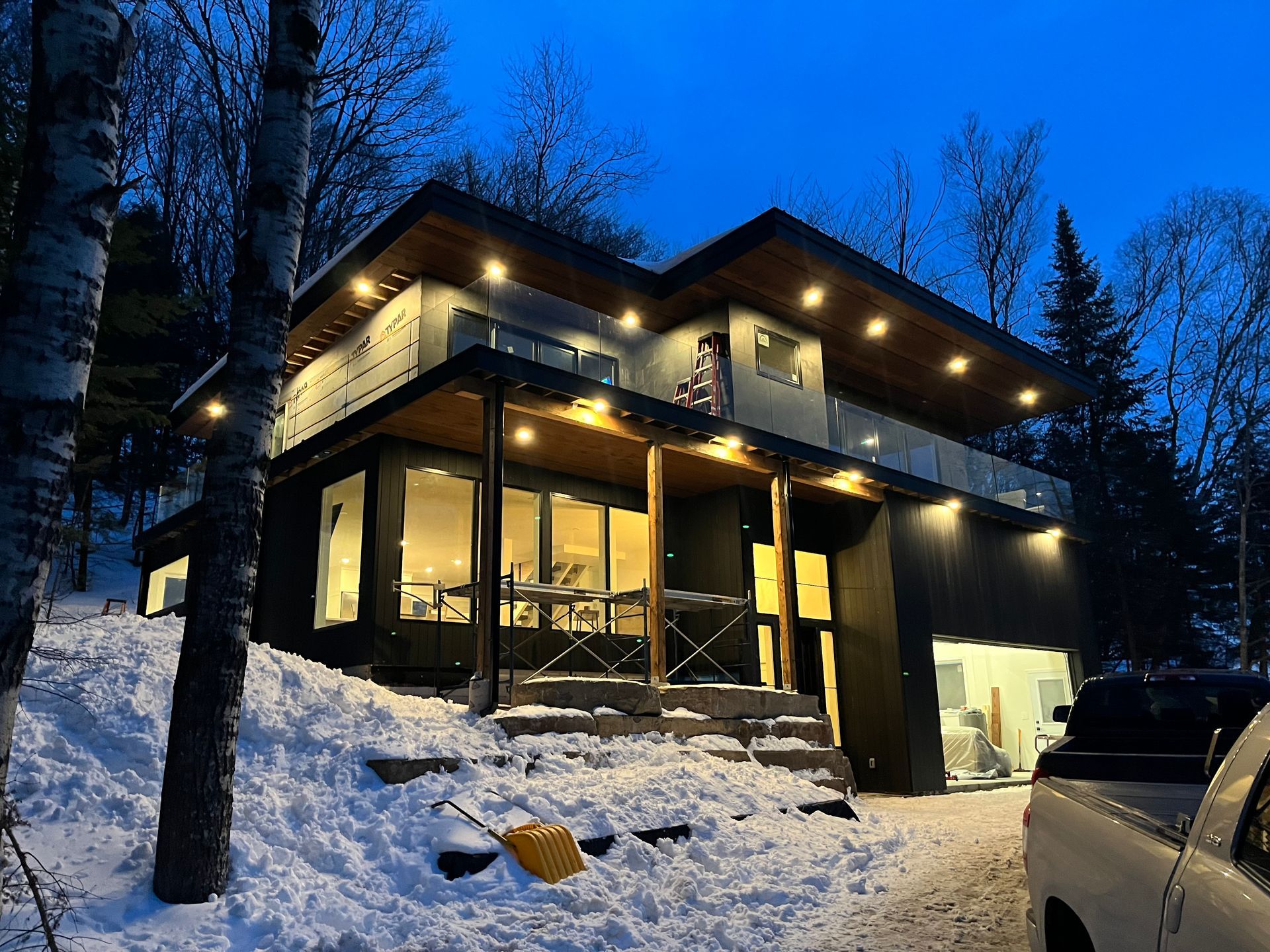 Snowy modern house at dusk with warm lights glowing and a car parked outside
