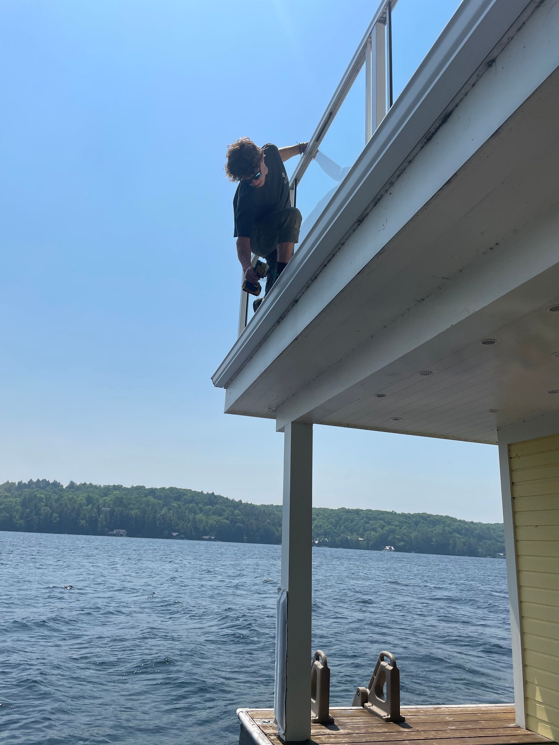 Person standing on a roof edge above a lake, with trees and water in the background.