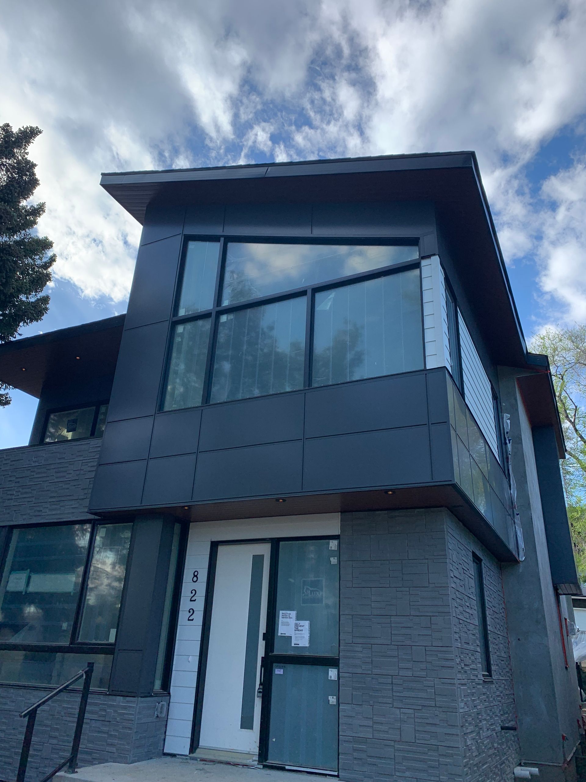 Modern two-story house with dark gray siding, large windows, and a brick lower facade under a cloudy sky