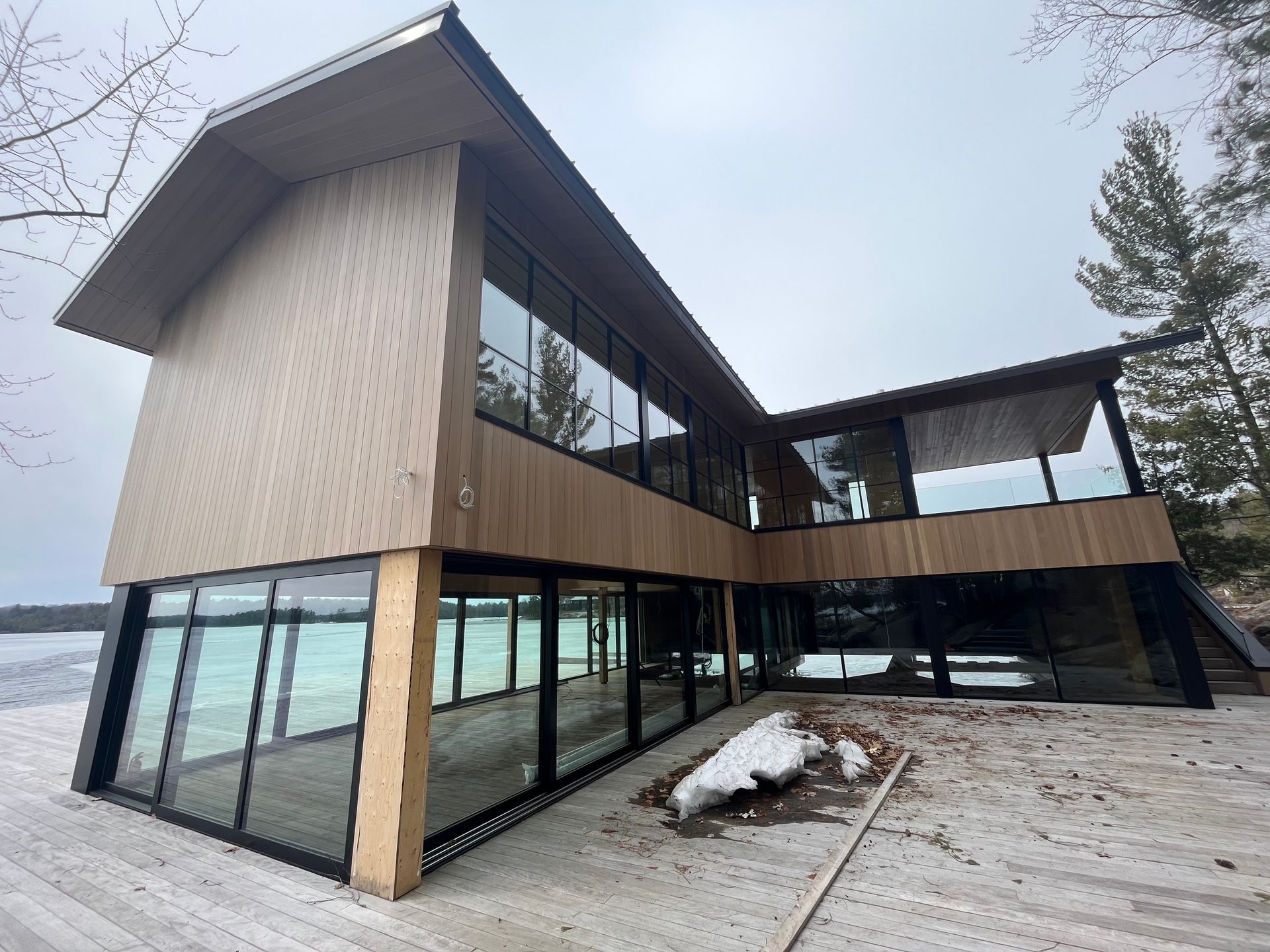Modern lakeside house with large windows and dark wood siding on snowy ground