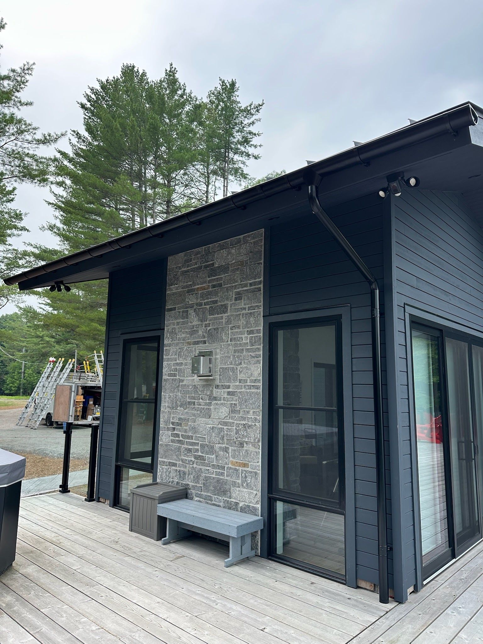 Modern black-and-stone cabin with large windows and a wooden deck surrounded by trees