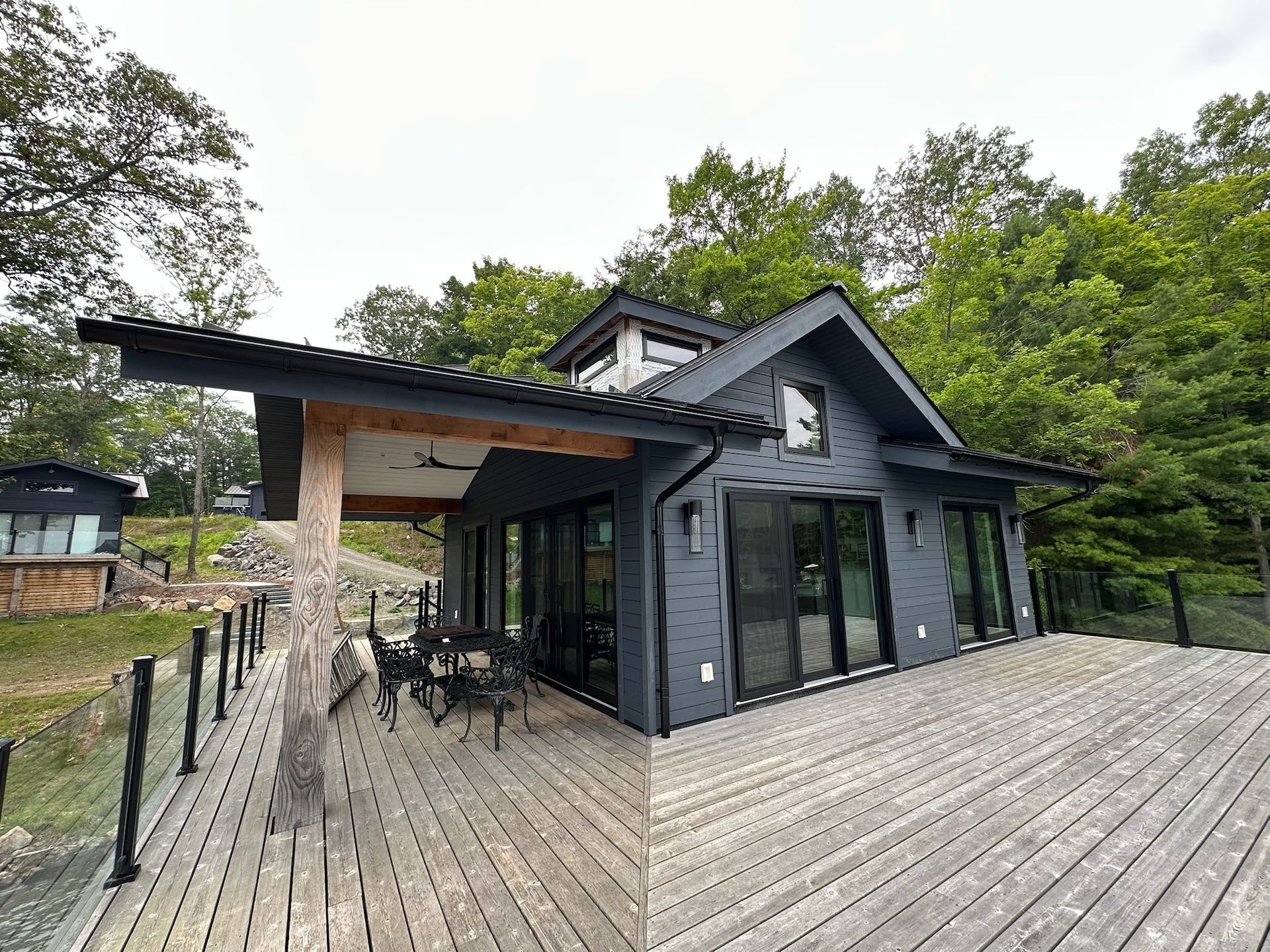 Modern dark-gray house with large windows and wood deck in a wooded setting