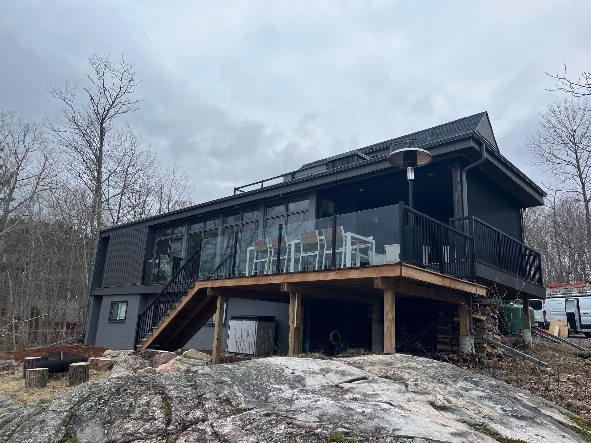 Modern cabin with dark wood exterior and glass railing on a rocky hillside under cloudy sky