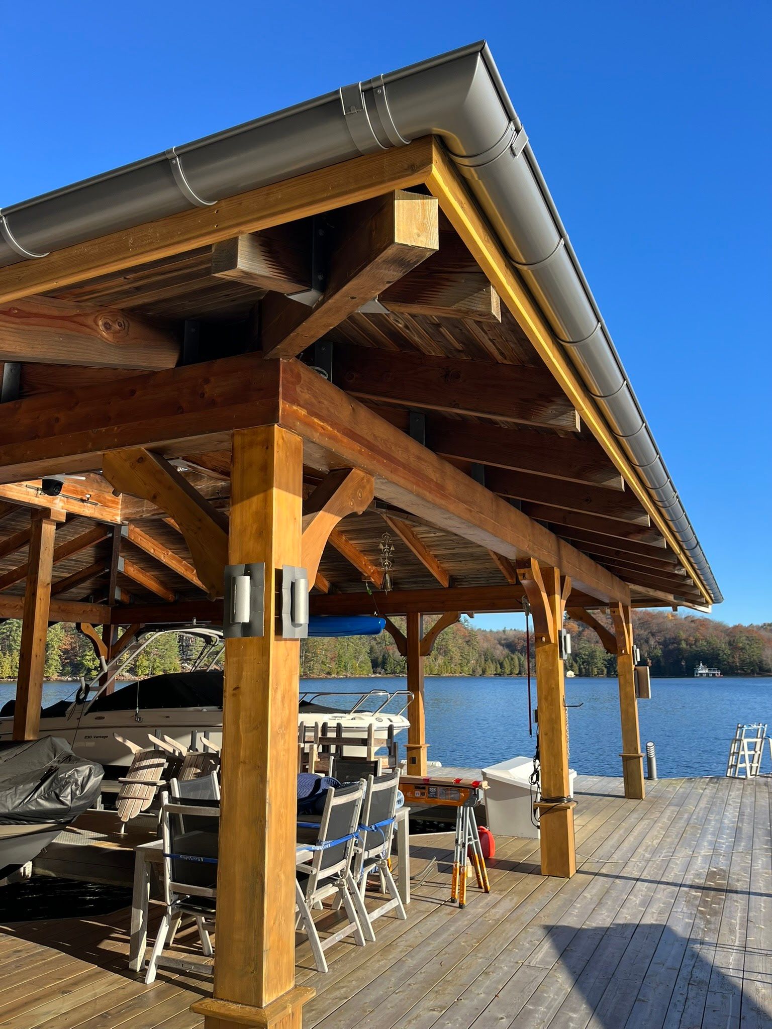 Wooden lakeside pavilion with tables and benches beside blue water on a sunny day