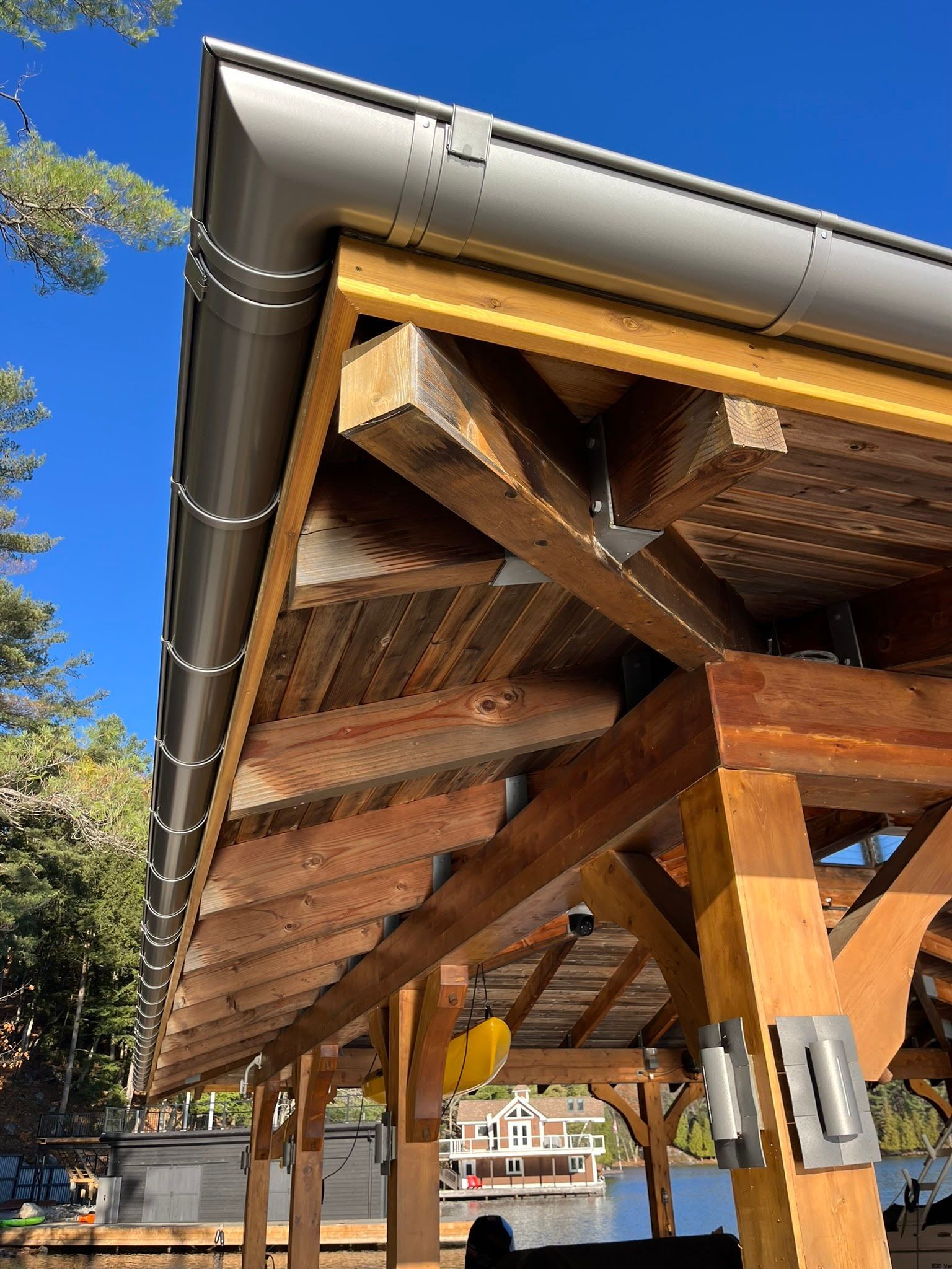Wooden pavilion roof with exposed beams and metal gutters against a blue sky