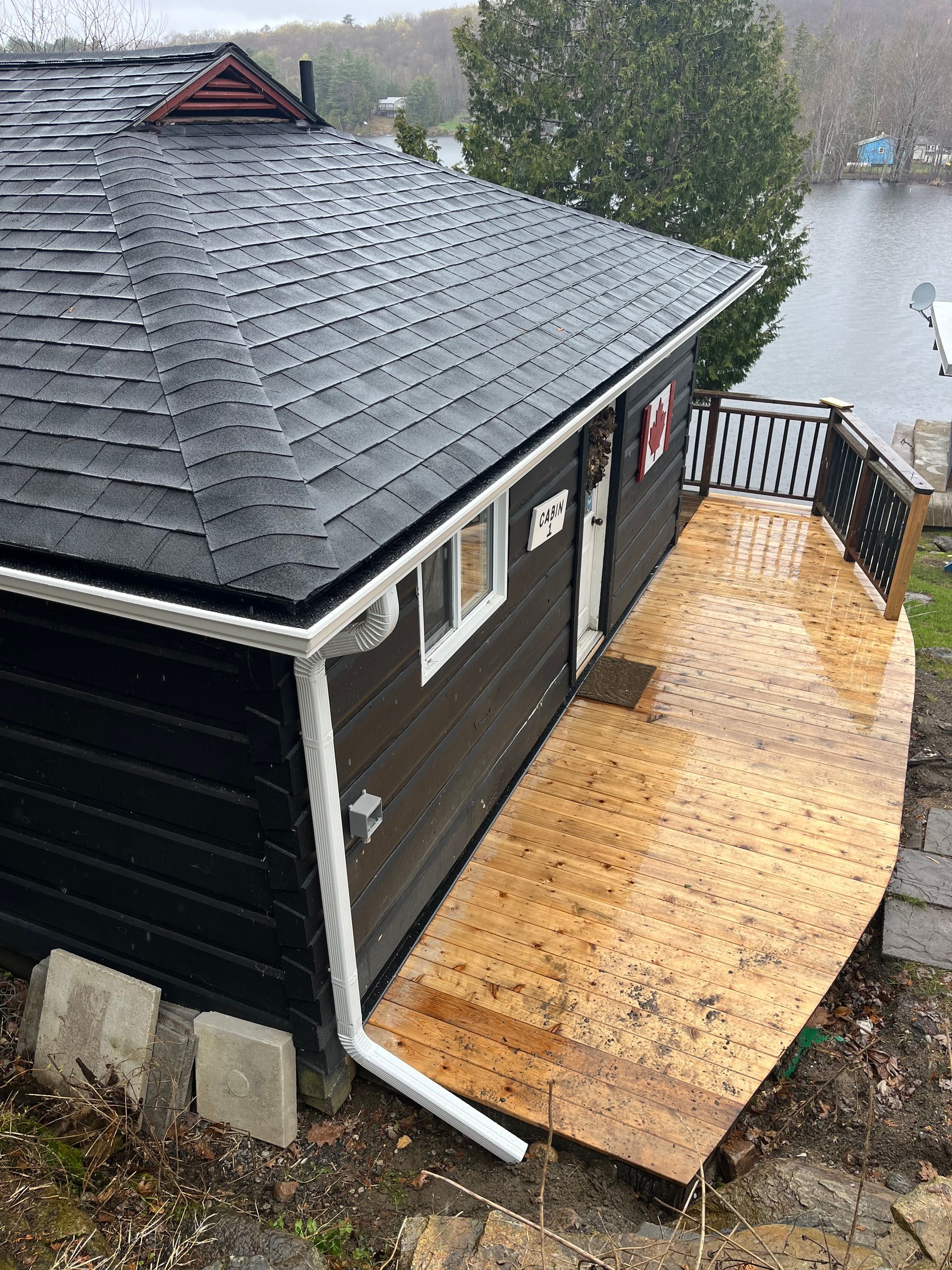 Black cabin with wet wooden deck overlooking water under gray skies