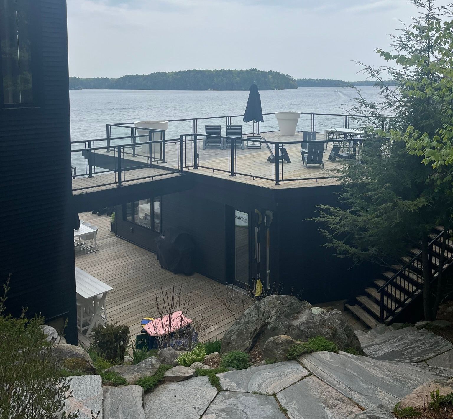 Lakeside deck with black railings, patio furniture, and stairs overlooking calm water and distant trees